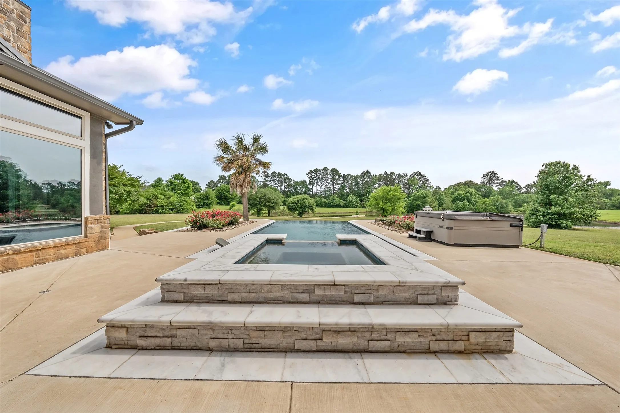 Outdoor patio featuring an integrated swimming pool and elevated spa, surrounded by concrete decking