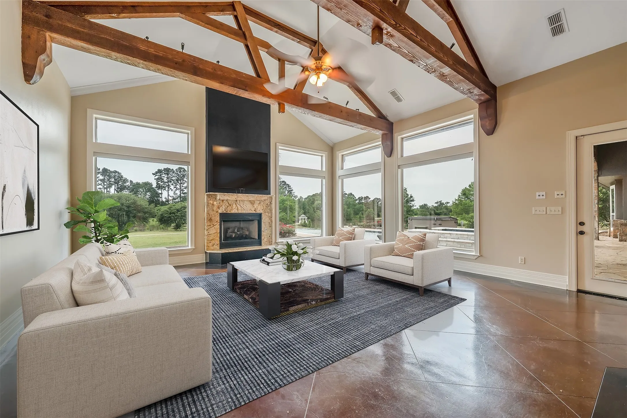 Vaulted ceiling with exposed wood beams, large picture windows, and a stone-clad fireplace with a dark hearth