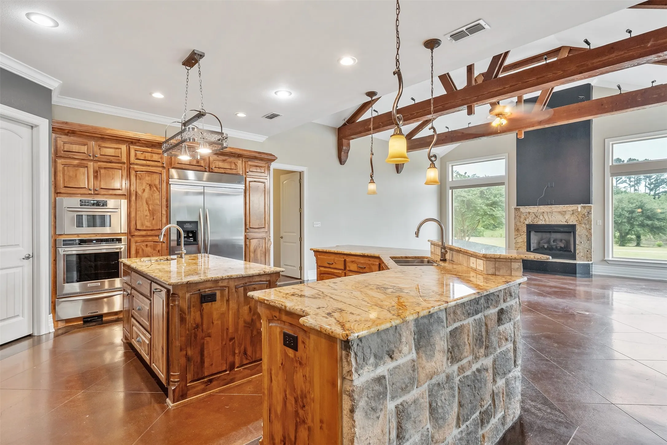 Kitchen featuring two islands with granite countertops, stainless steel appliances, wood cabinetry, and a stone-clad island base