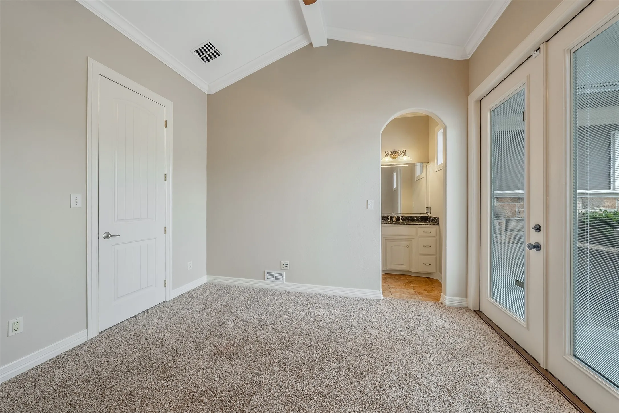 Vaulted ceiling with white crown molding, light-colored carpet flooring, and a six-panel interior door