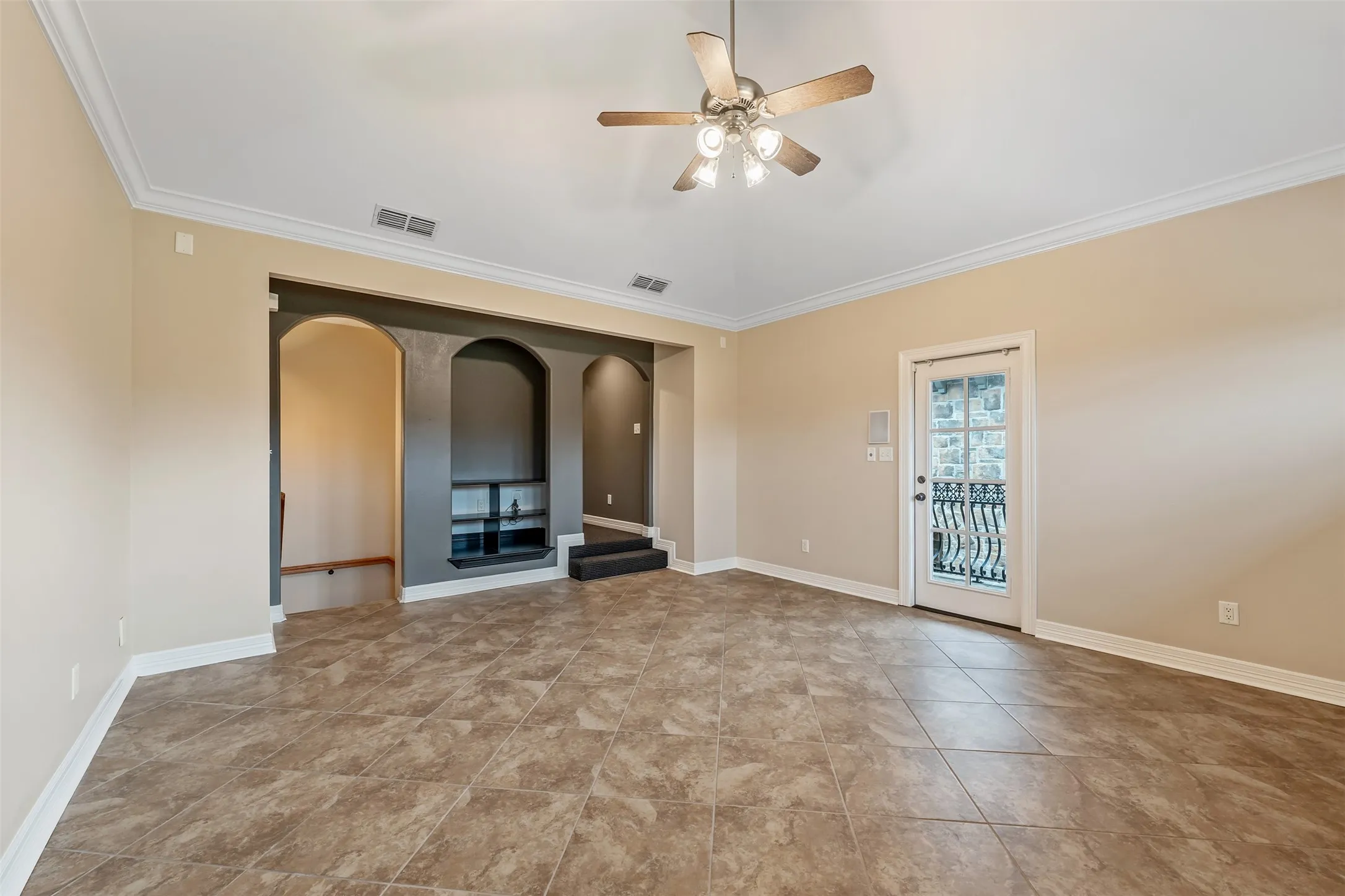 Spacious room featuring tile flooring, crown molding, a ceiling fan with integrated lighting, and a built-in entertainment niche with arched shelving