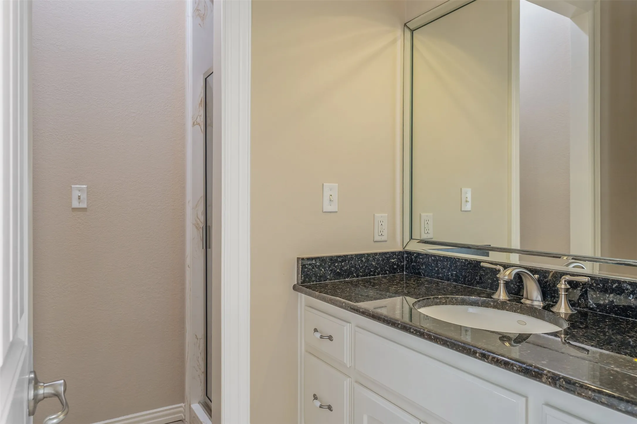 Bathroom vanity with an undermount sink, brushed nickel faucet, and a black speckled countertop