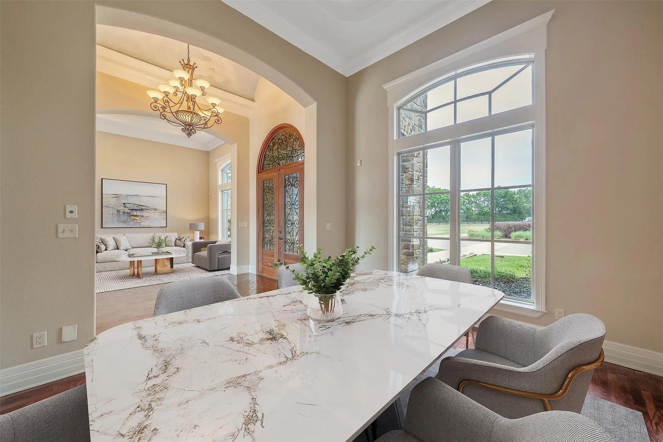 Dining area featuring a large arched window with grid-patterned panes, a white marble-finish table, and light-toned walls