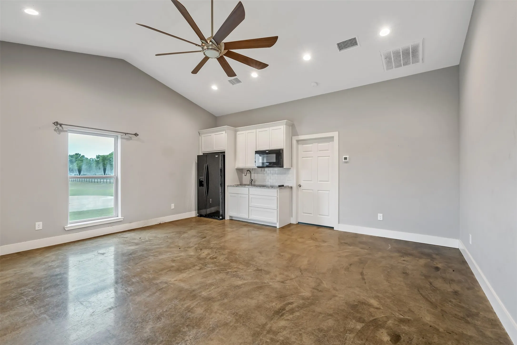 Open-concept living space with stained concrete flooring, vaulted ceilings, and recessed lighting