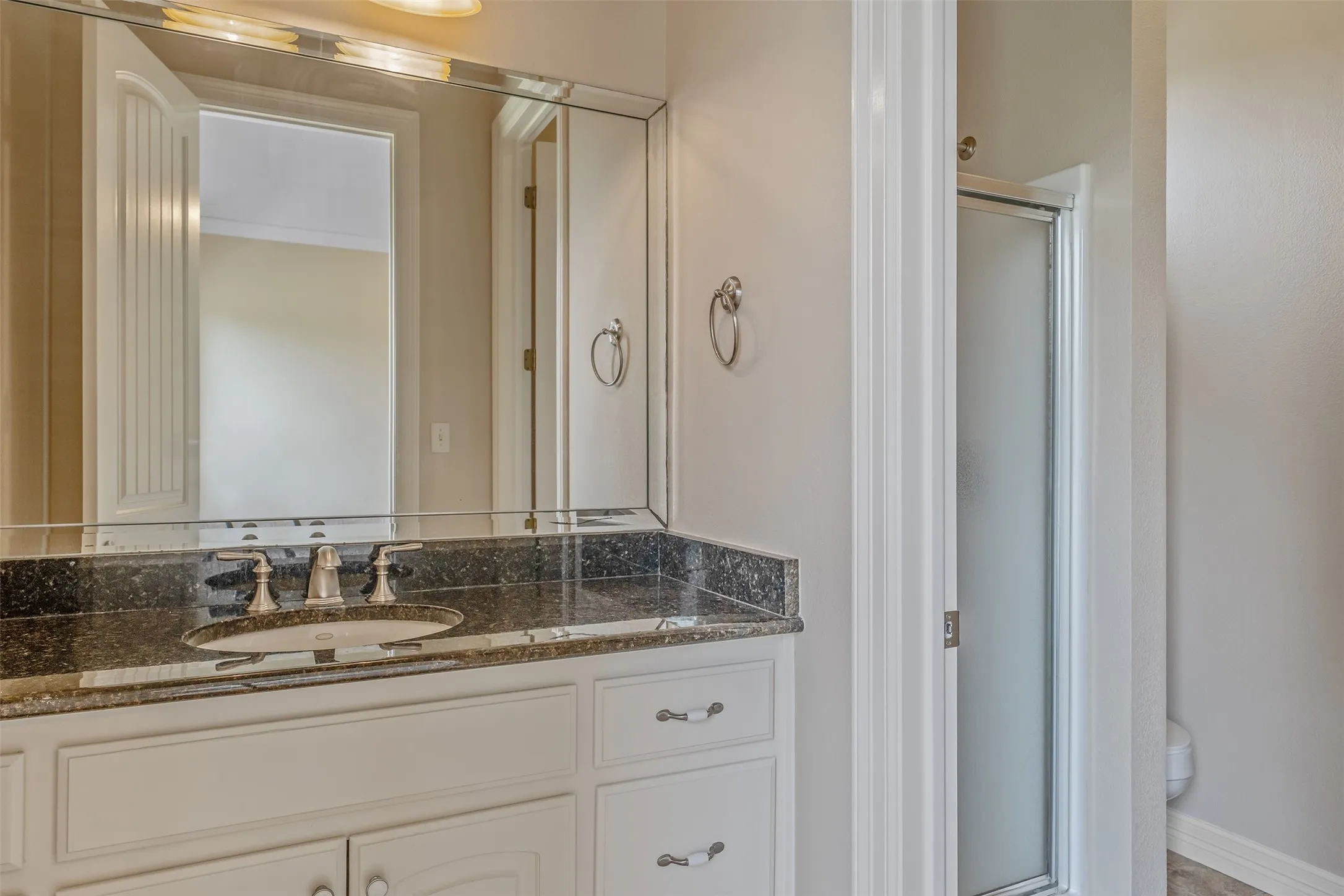 Bathroom vanity featuring a dark speckled countertop, undermount sink, brushed nickel faucet, and a large framed mirror with beveled edges