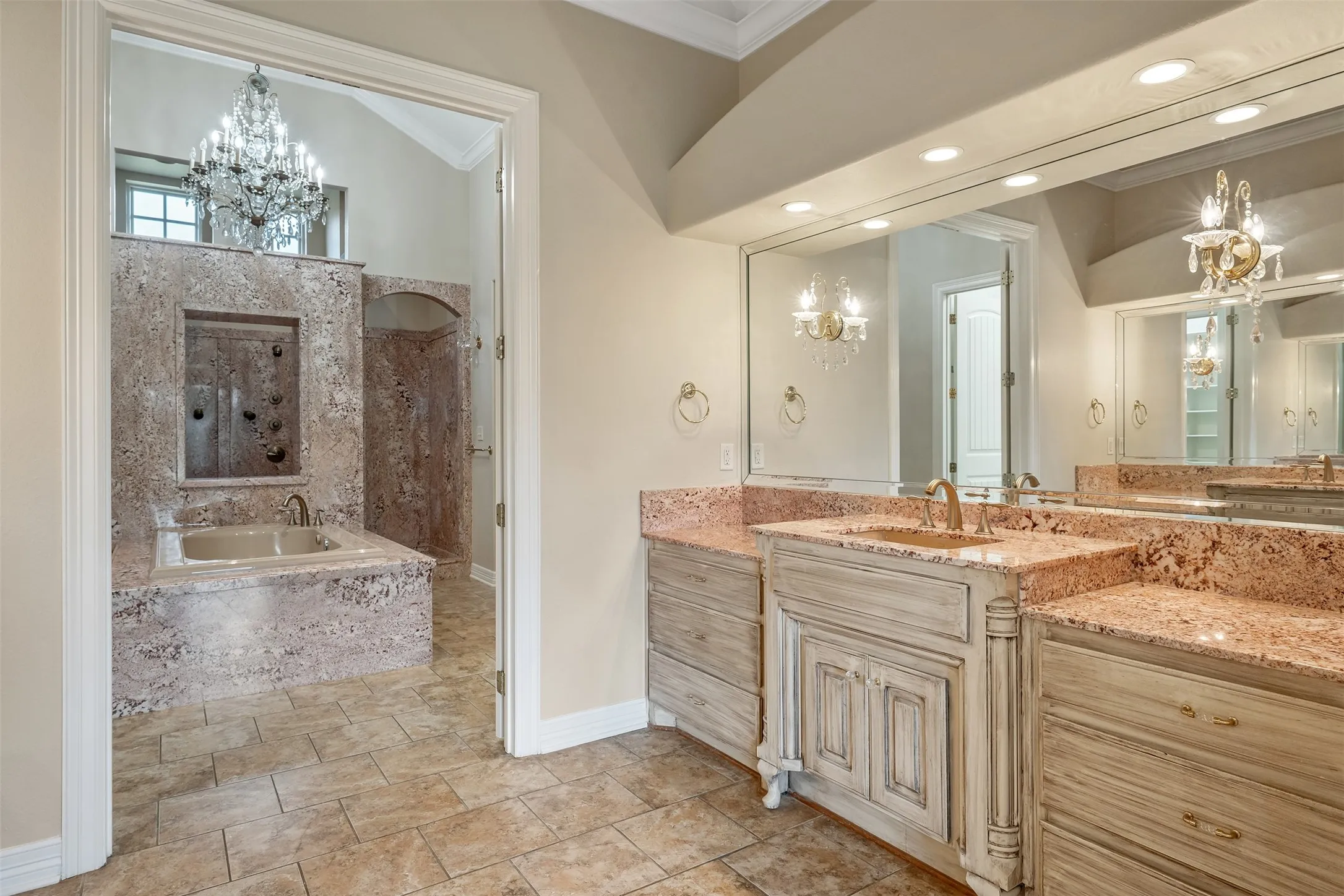 Double vanity with stone countertops and integrated sinks, extensive wall mirror, and ornate sconces