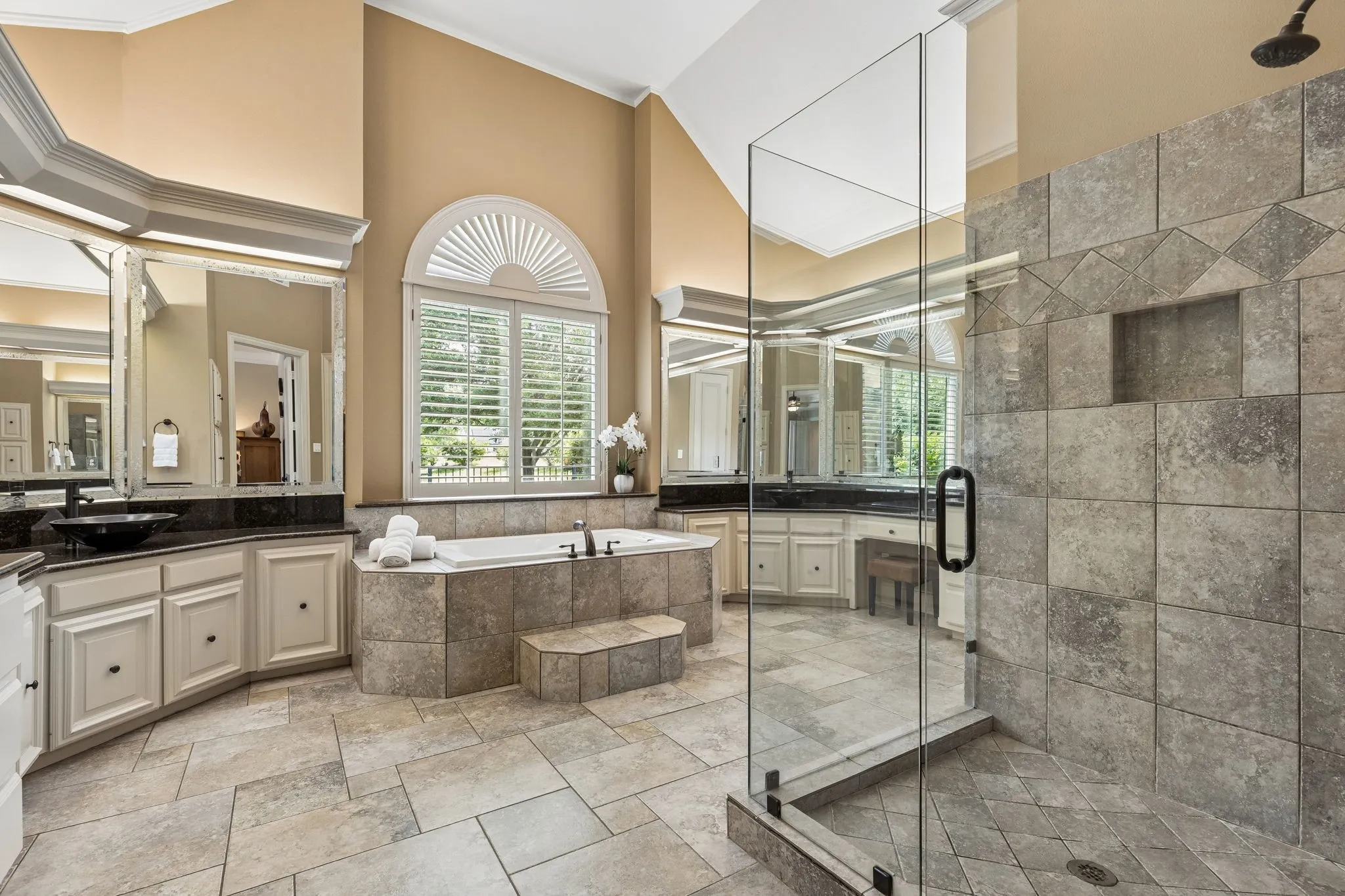 Primary spa bath with extensive counter space, separate vanities, vaulted ceilings, and frameless glass walk-in shower.