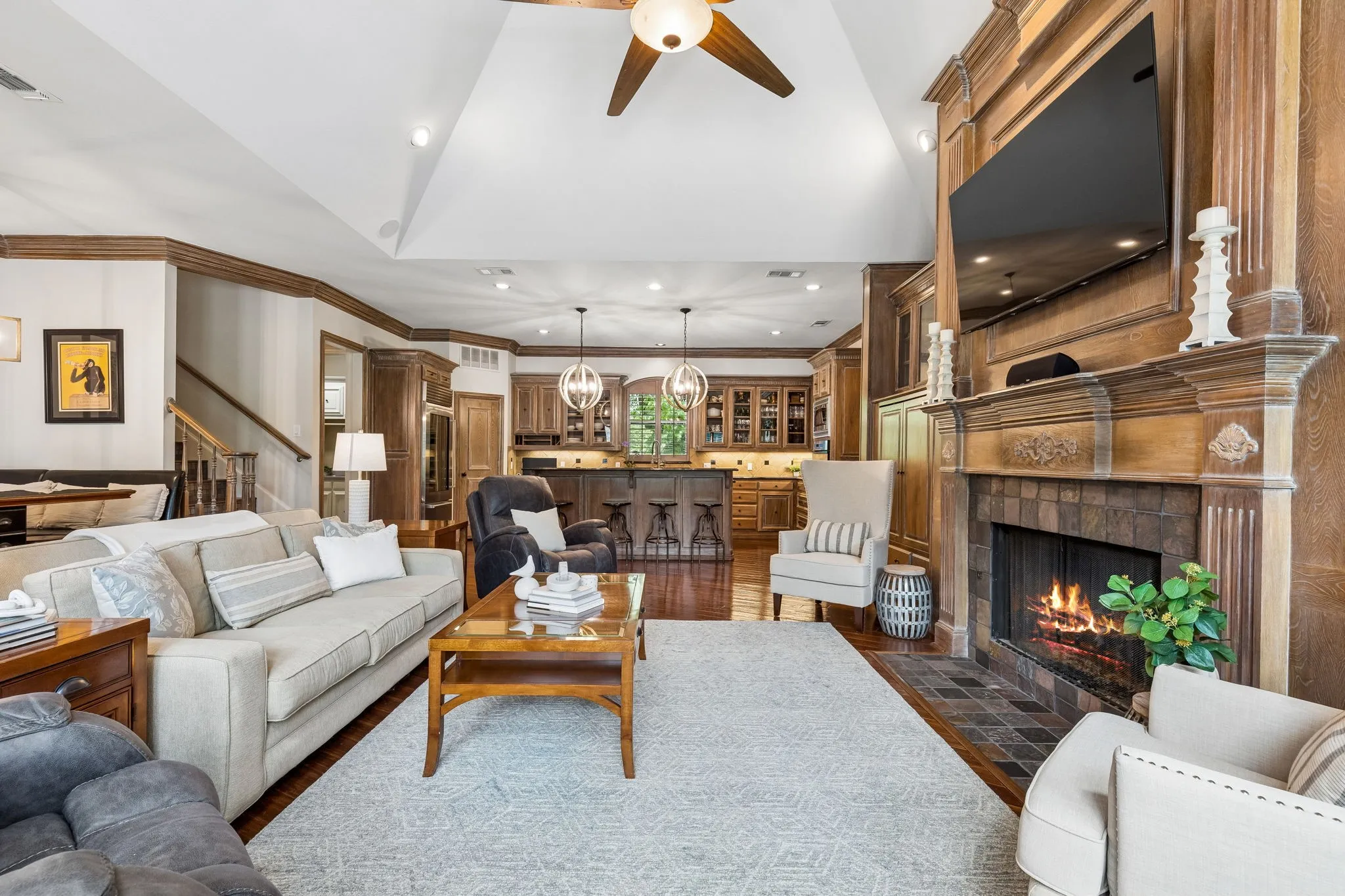 Natural light fills the family room with soaring vaulted ceilings, grand fireplace, custom built-ins, charming window seat, wet bar with built-in wine fridge, and a wall of windows overlooking the outdoor living area, pool, and private backyard.