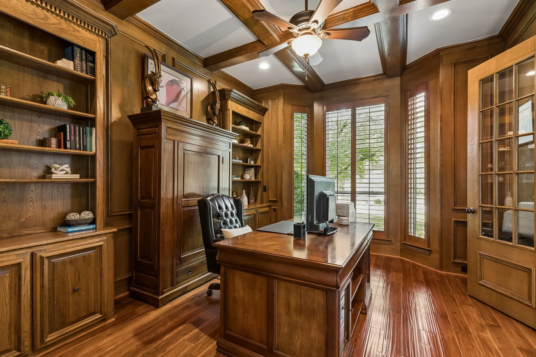 Double doors lead to the executive office featuring custom woodwork, built-in shelving, and coffered ceiling.