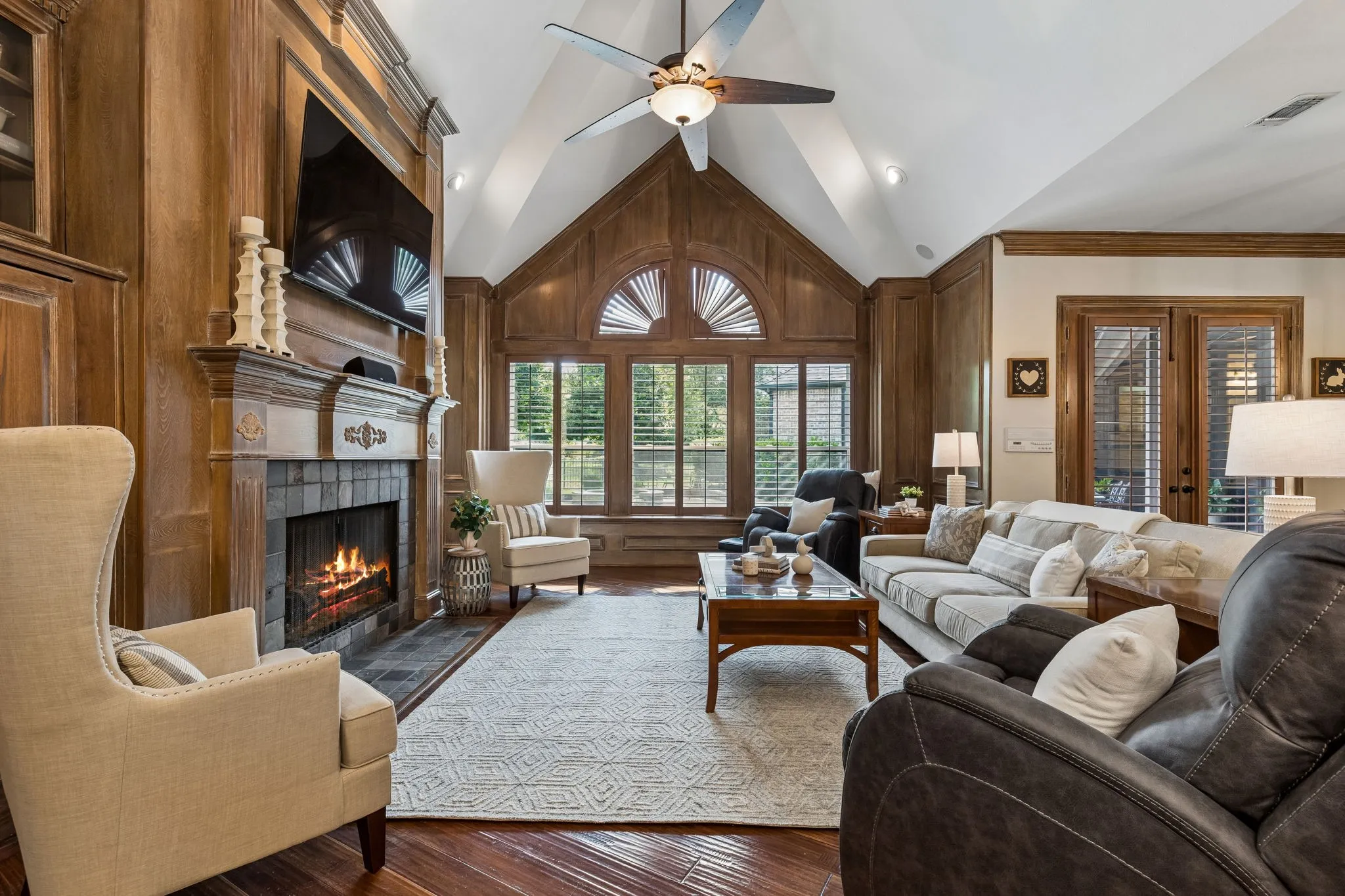 Natural light fills the family room with soaring vaulted ceilings, grand fireplace, custom built-ins, charming window seat, wet bar with built-in wine fridge, and a wall of windows overlooking the outdoor living area, pool, and private backyard.