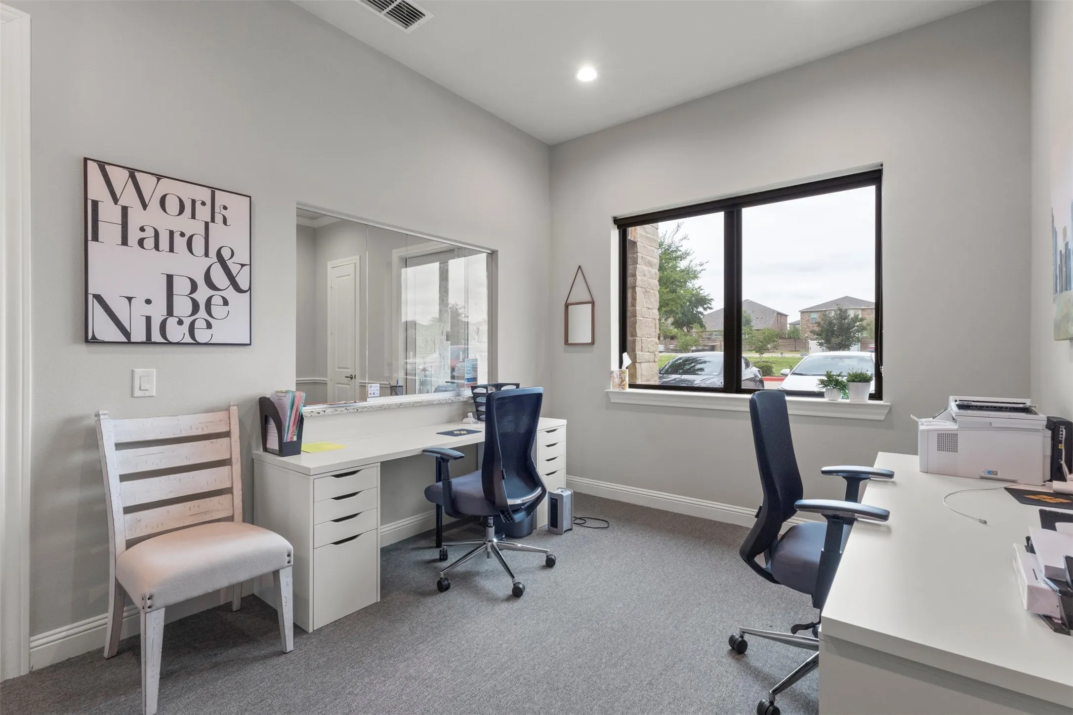 Dedicated office space featuring a large window, recessed lighting, neutral wall paint, gray carpet flooring, and a built-in pass-through opening