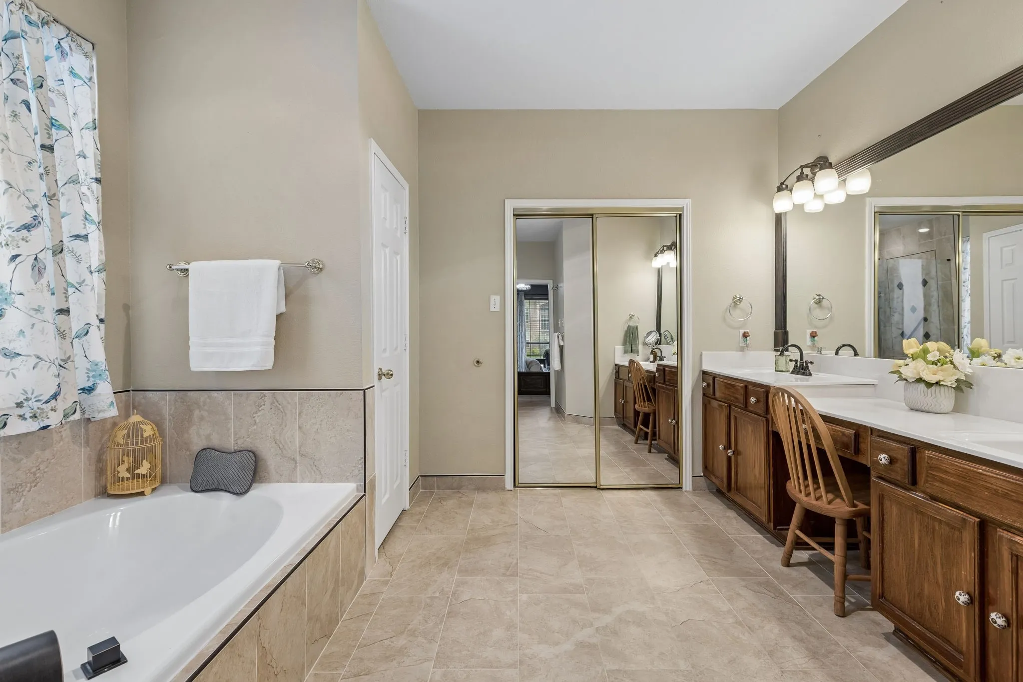 Spacious updated bathroom featuring neutral tile flooring, a built-in bathtub with tiled surround, with dual sinks, and wood-finish cabinetry