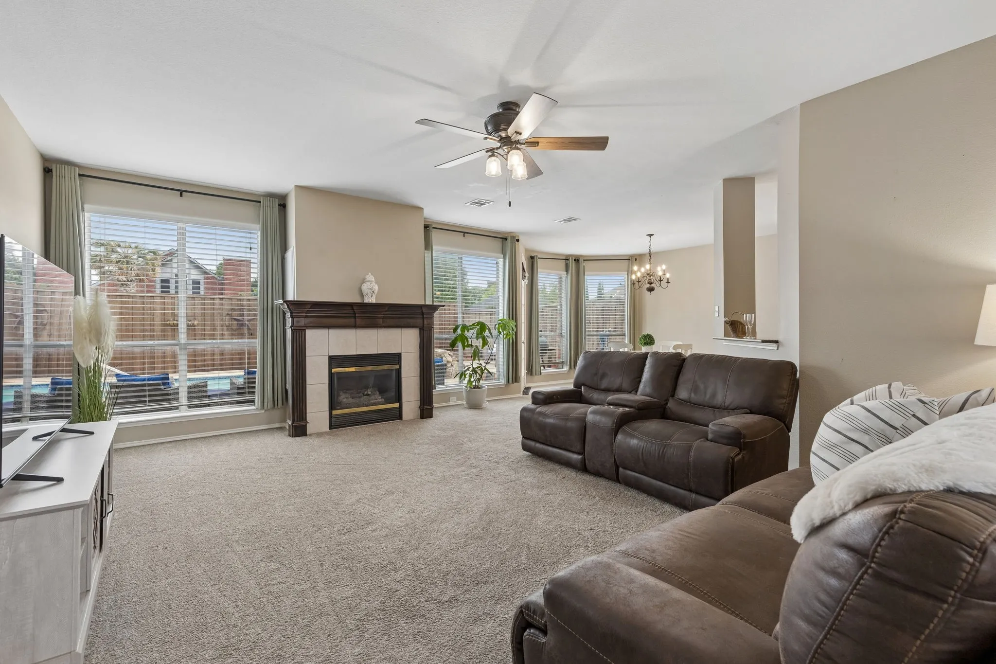 Living area featuring a fireplace with a dark wood mantel and a tile surround, large windows, and neutral carpeting