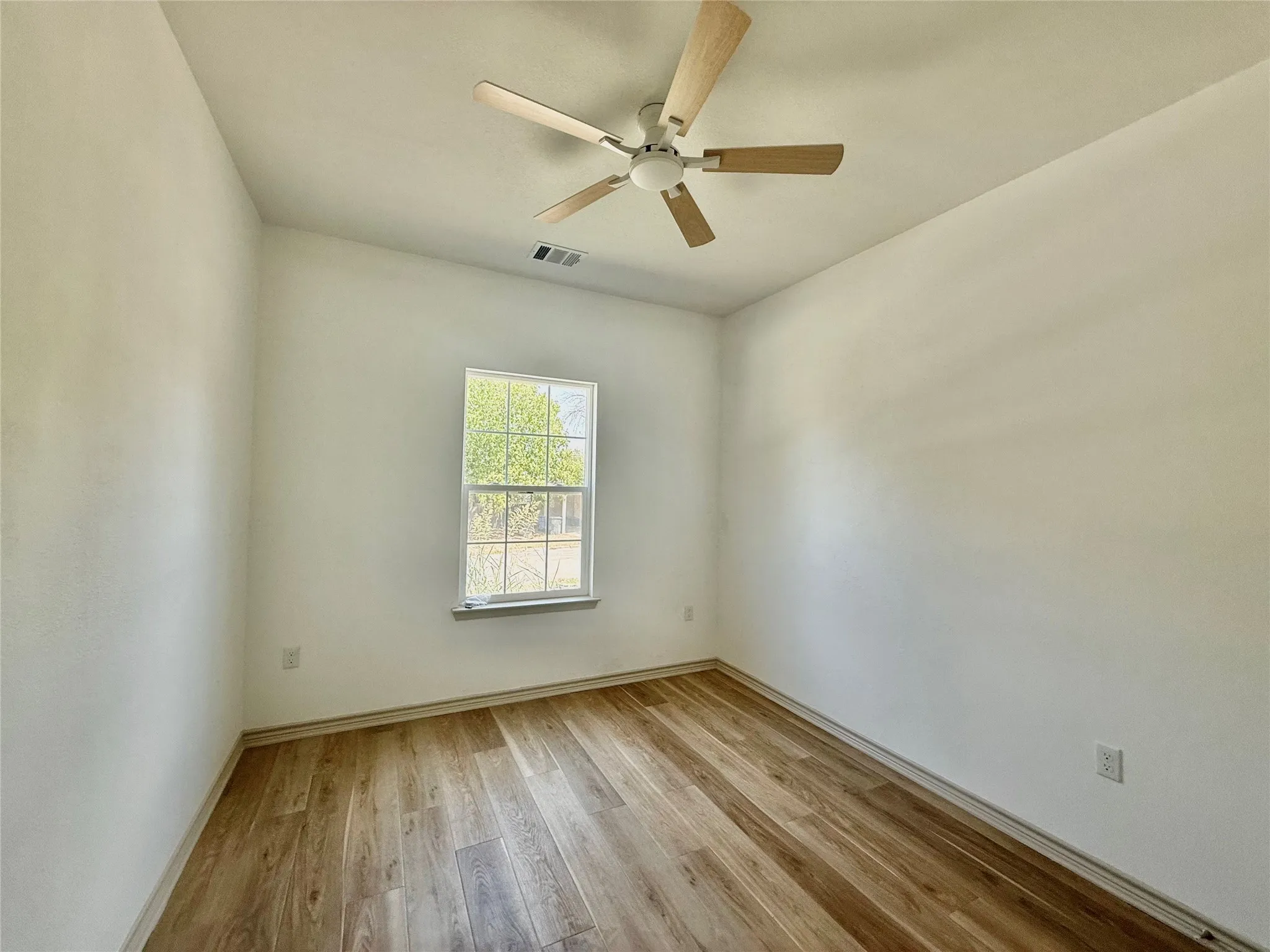 Wood-finish flooring, white walls, double-hung window, and a ceiling fan with wood-tone blades