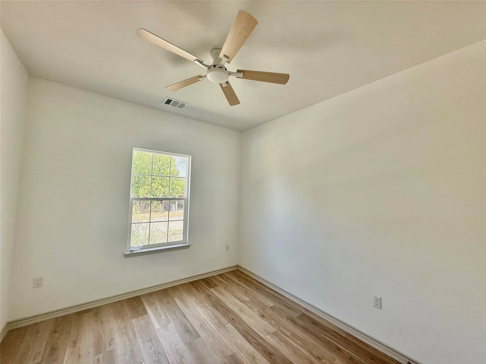 Wood-finish flooring, white walls, ceiling-mounted fan with light fixture, and a single window