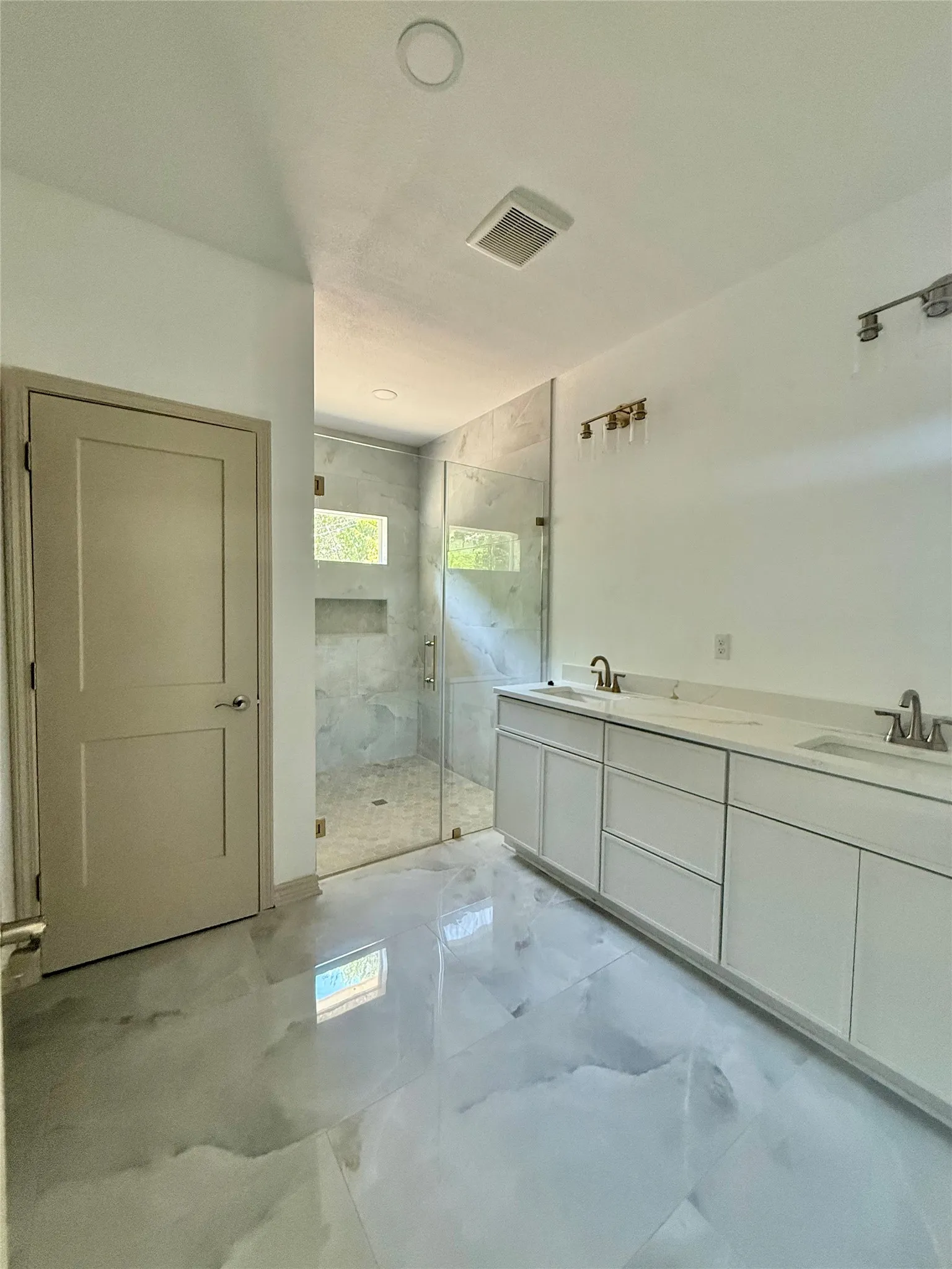 Dual vanity with undermount sinks, frameless glass shower enclosure, recessed shower niche, large format tile flooring, and overhead recessed lighting