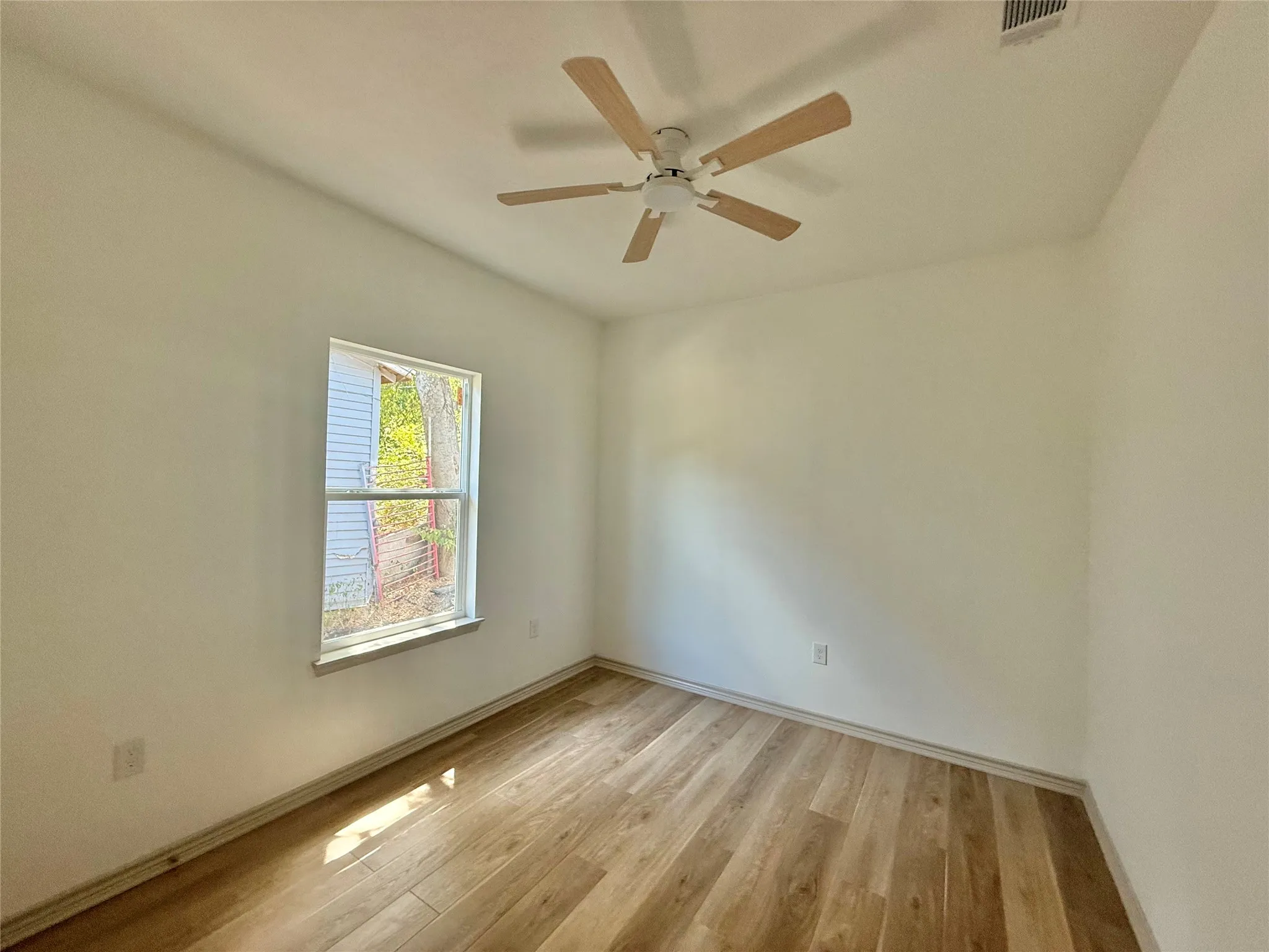 Wood-finish flooring, white painted walls, single window, and a ceiling fan with light fixture