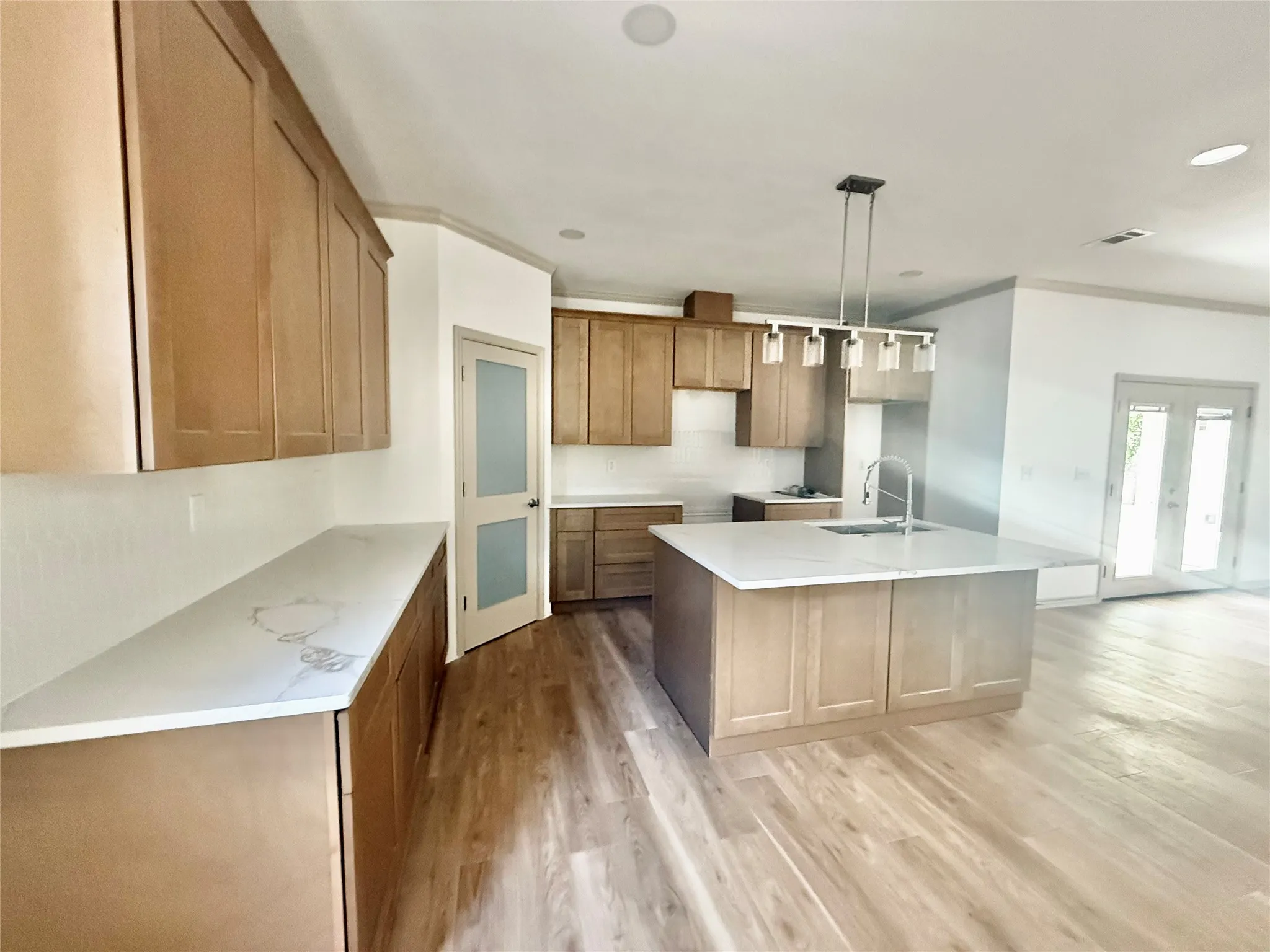 Kitchen featuring light wood-finish cabinetry, white countertops, a central island with an undermount sink, a subway tile backsplash, and light wood-finish flooring