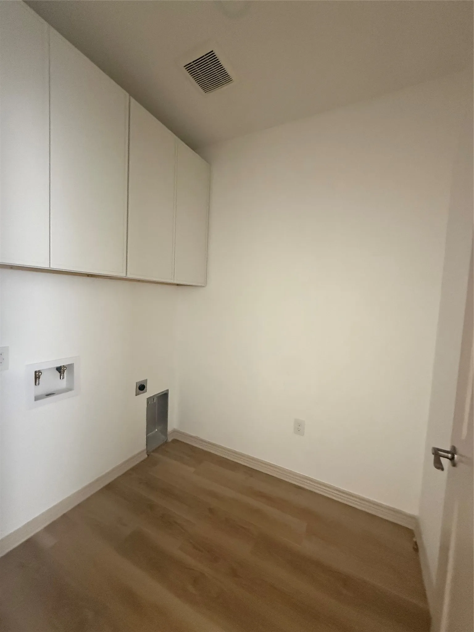 White cabinetry, wood-finish flooring, white walls, and a white door with a silver-finish handle