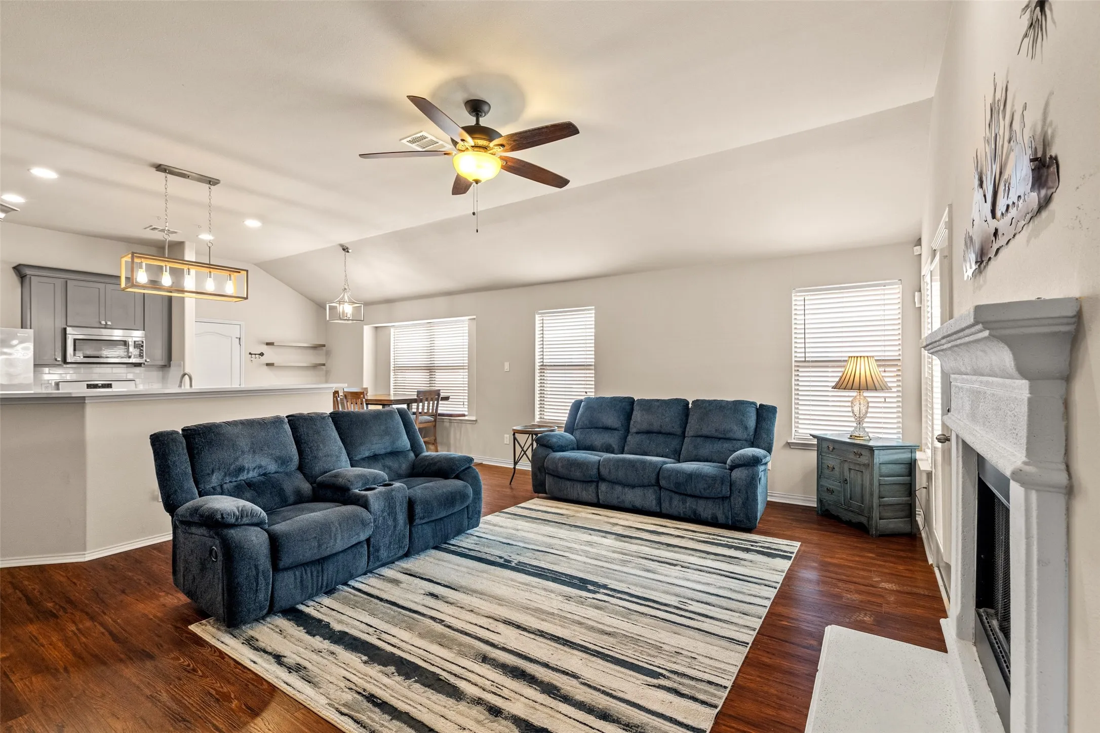 Spacious living area featuring wood-finish flooring, a white mantel, and a ceiling fan