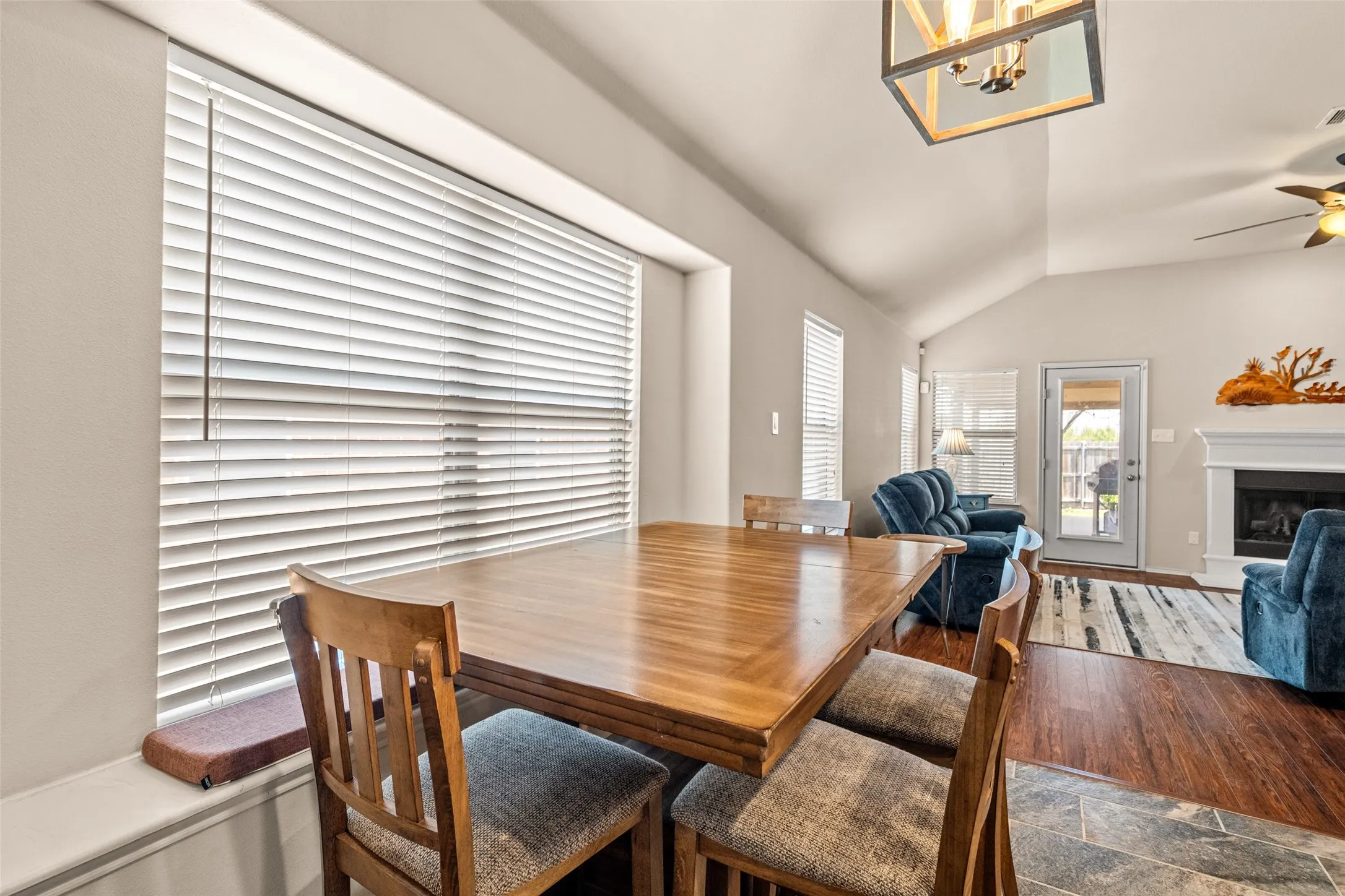 Dining area featuring a large window with blinds, wood-finish flooring, and vaulted ceiling