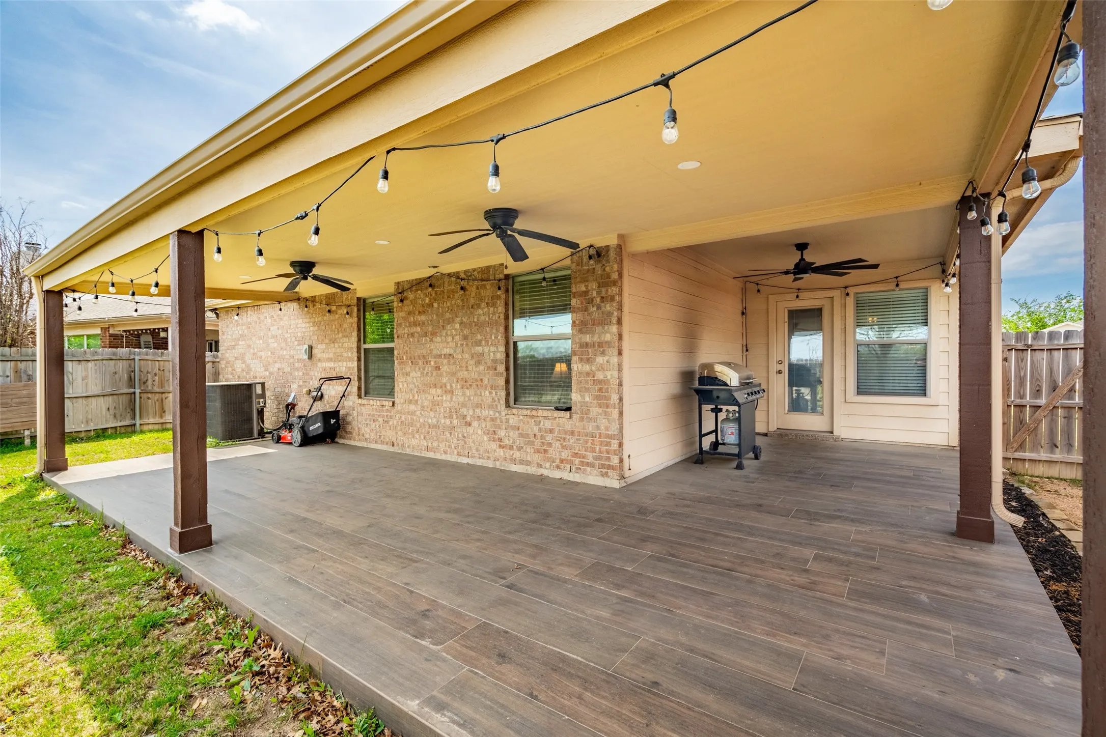 Expansive covered patio featuring wood-finish flooring, recessed ceiling fans, string lighting, and brick and siding exterior walls