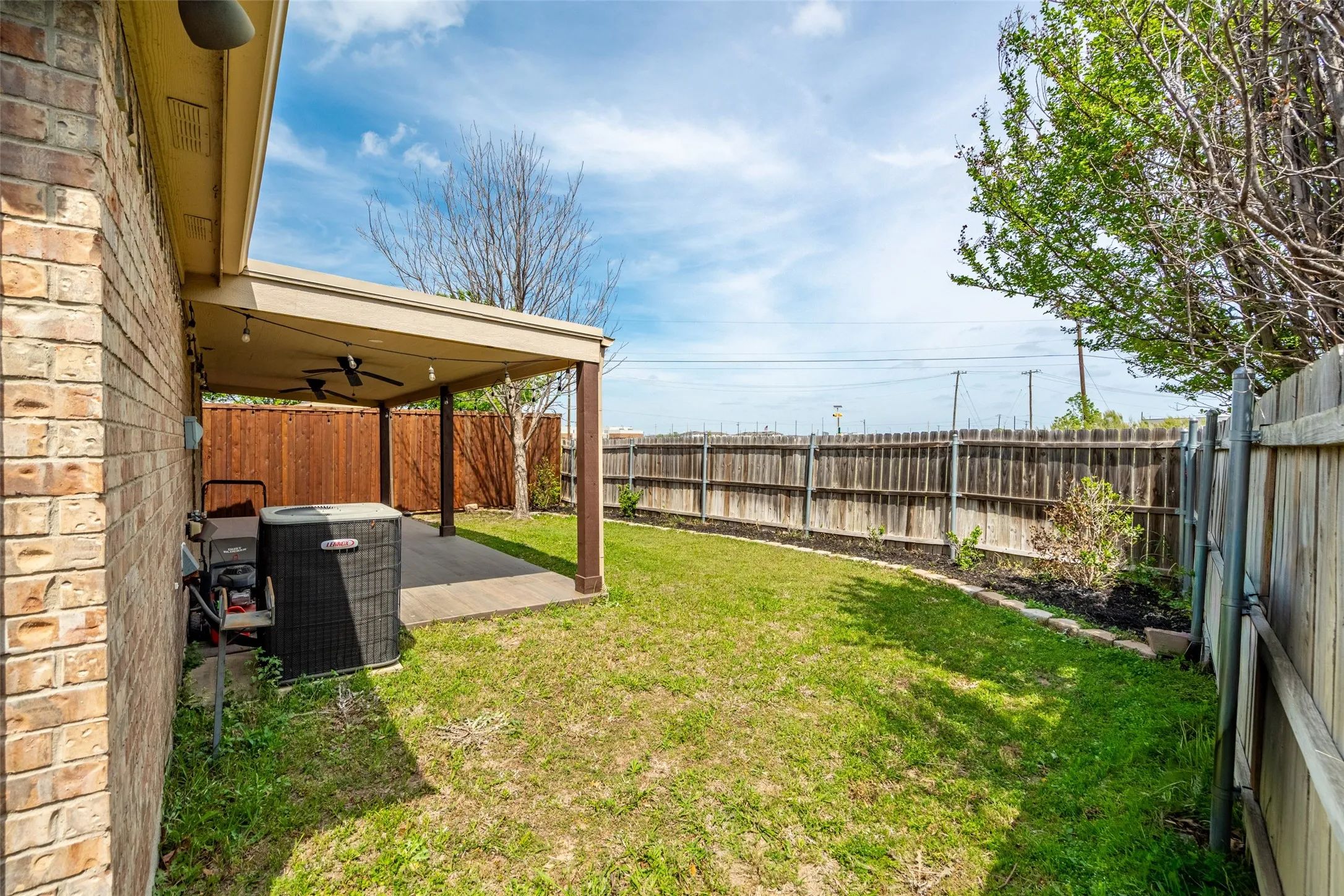 Expansive backyard featuring a covered patio with ceiling fans and string lights, a brick exterior, and a wood fence enclosing a grassy area
