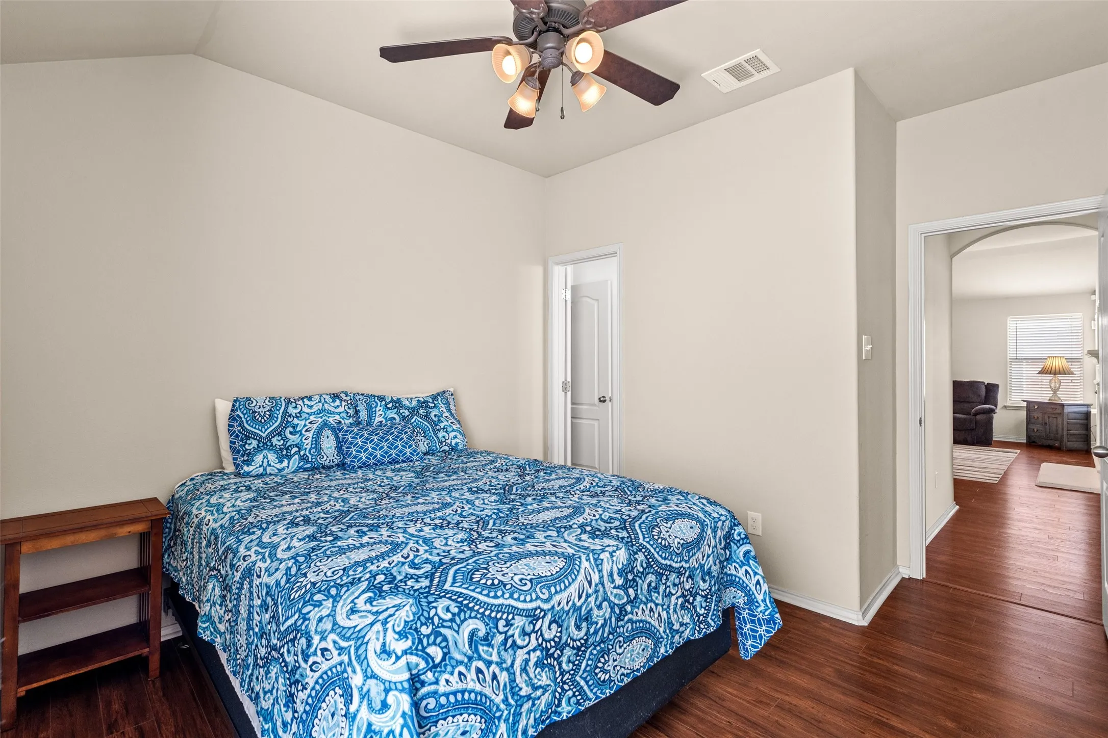 Vaulted ceiling room featuring wood-finish flooring, a ceiling fan with light fixture, and neutral wall tones