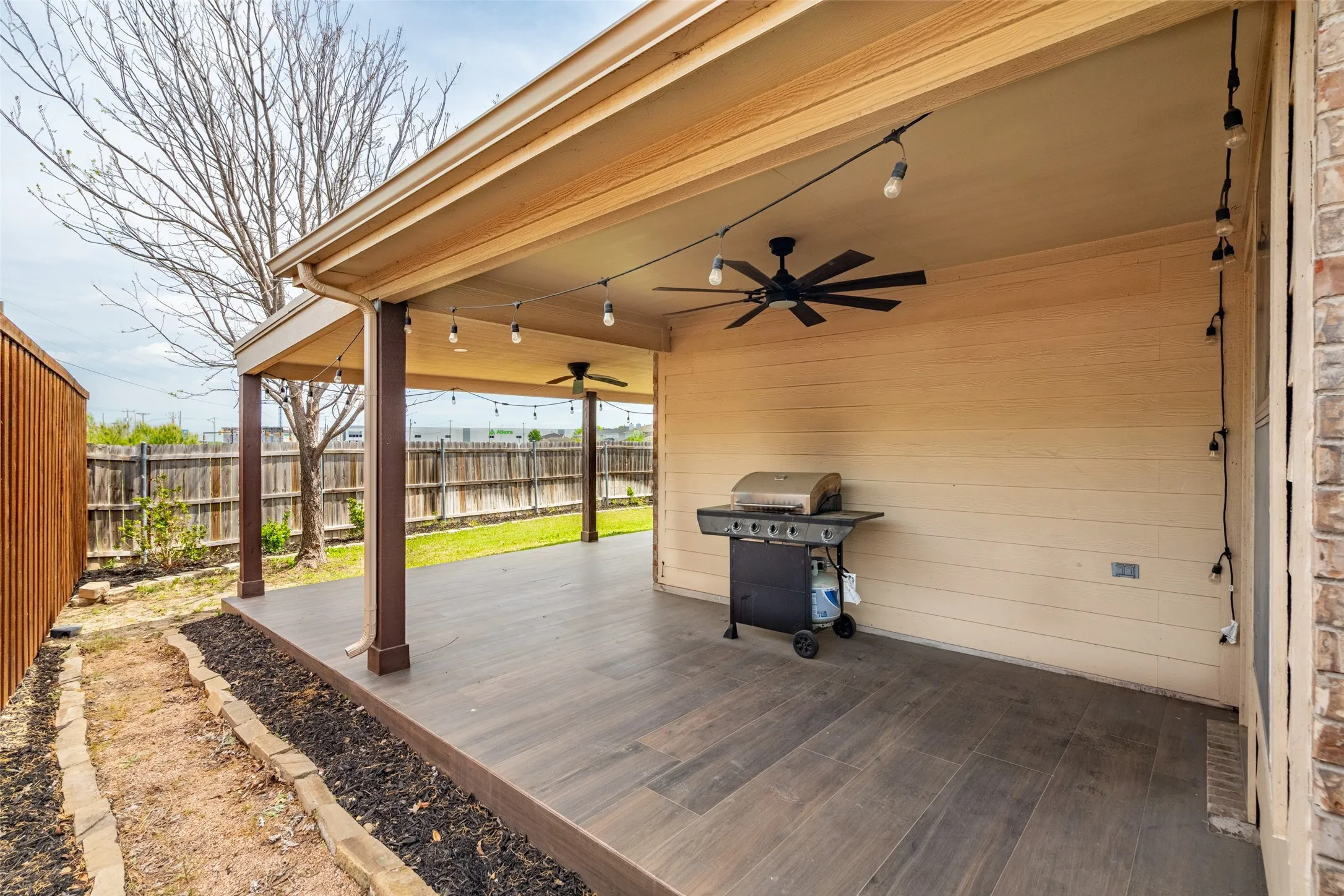 Expansive covered patio featuring dark wood-finish flooring, two ceiling fans, and string lighting