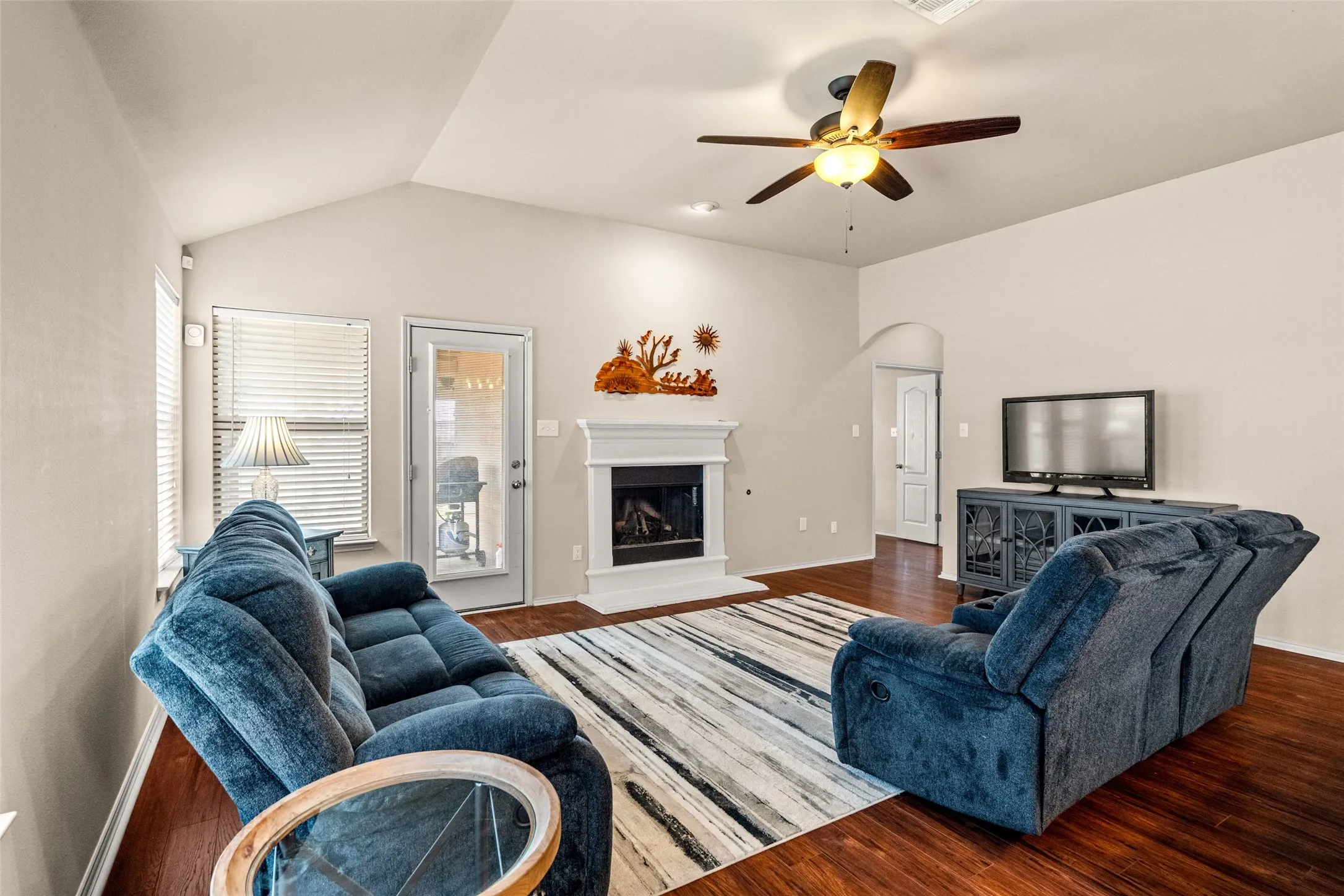 Living area featuring wood-finish flooring, vaulted ceilings, and a fireplace with a white mantel