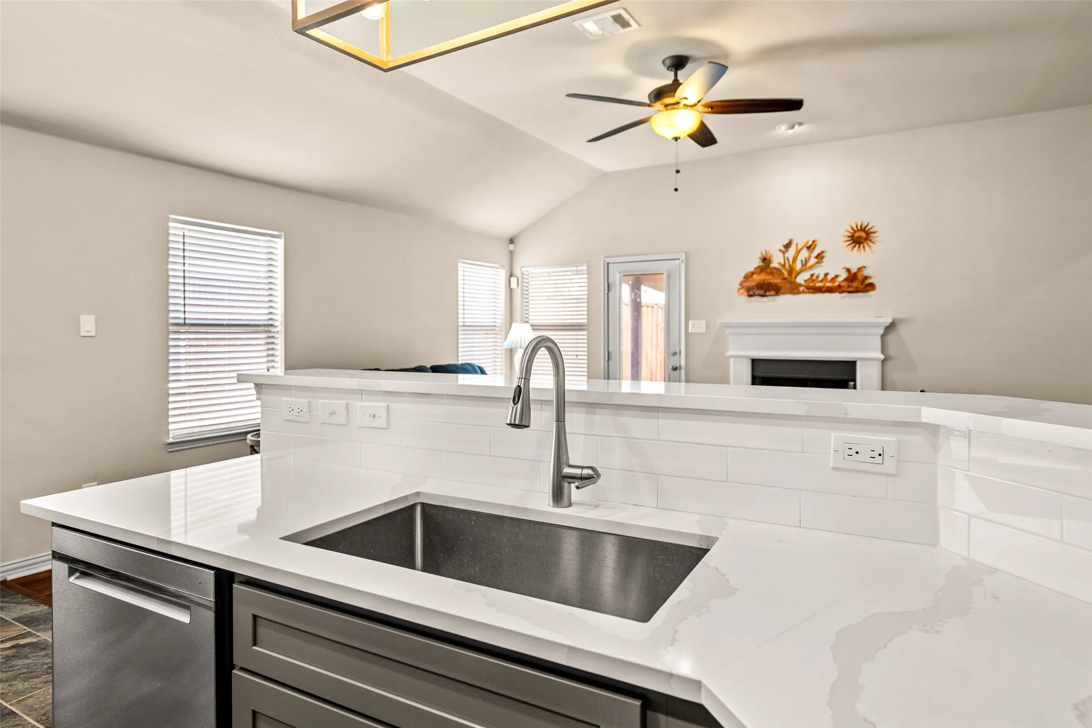 Kitchen island featuring a stainless steel sink, gooseneck faucet, light-toned countertop, and white subway tile backsplash