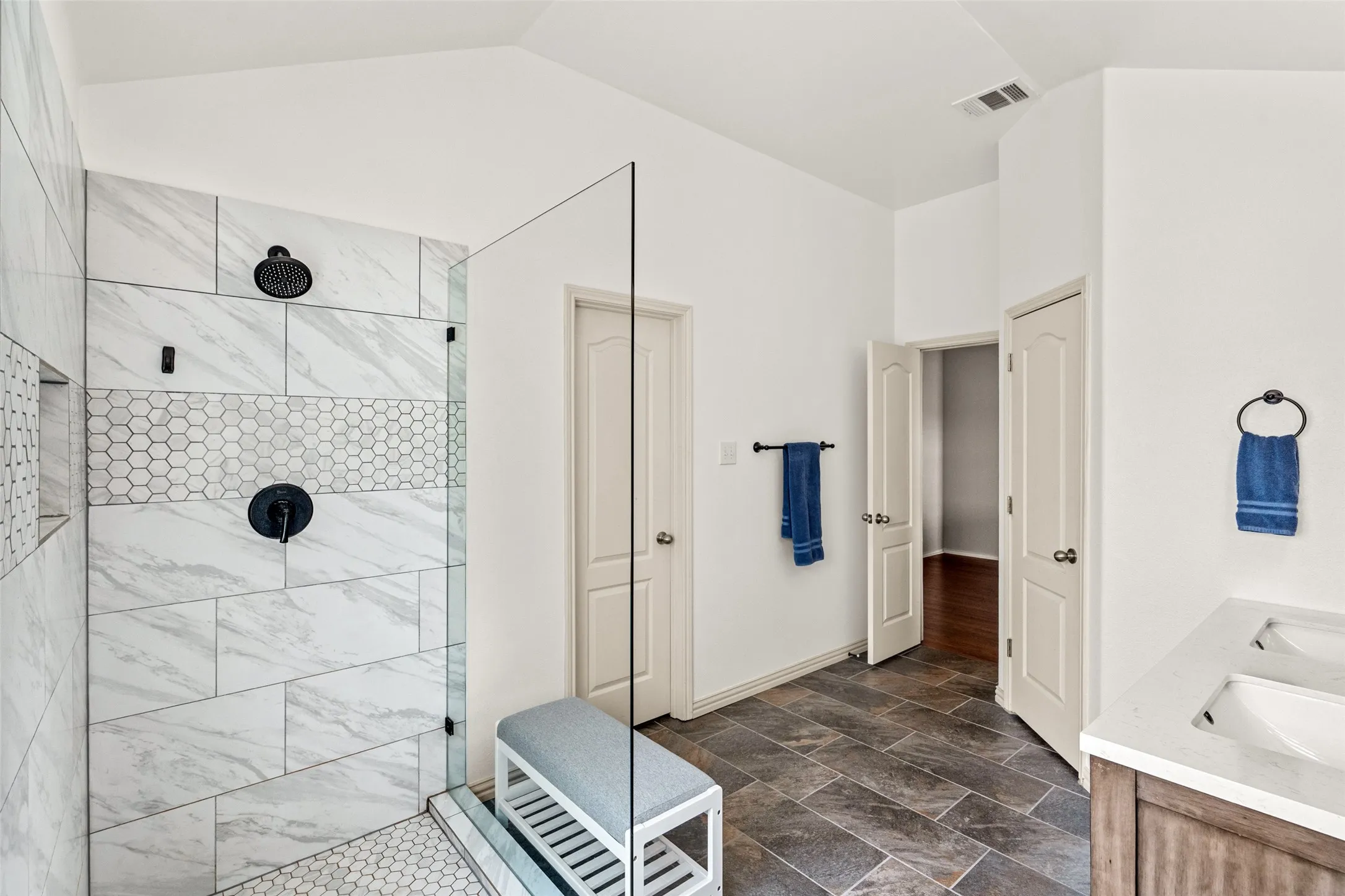 Walk-in shower featuring large format white marble-look tile, a mosaic hexagon tile accent band, and matte black fixtures