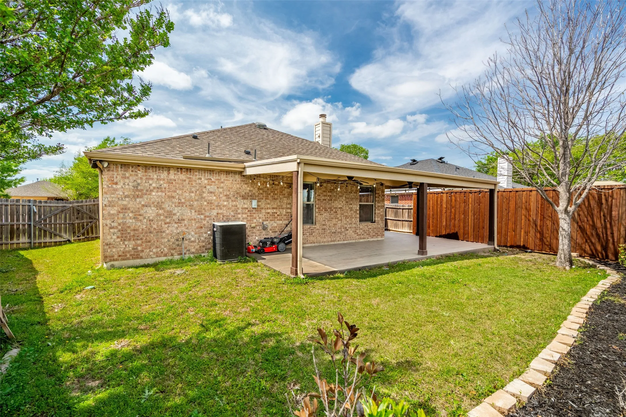 Spacious brick home featuring an expansive covered patio, established lawn, and stone-edged landscaping beds