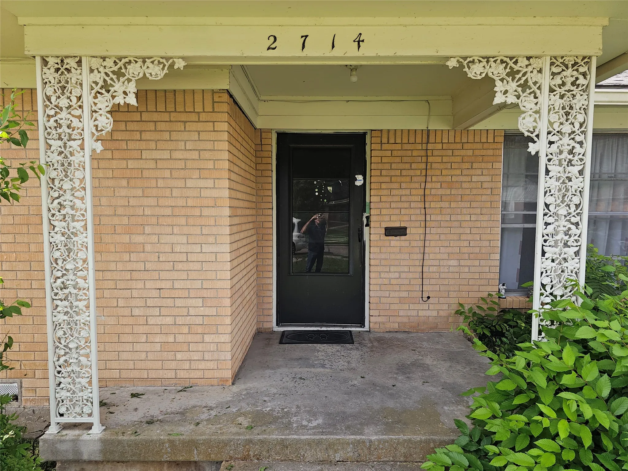 Covered front entry featuring ornate white ironwork columns, a dark entry door with glass paneling, and a light brick facade
