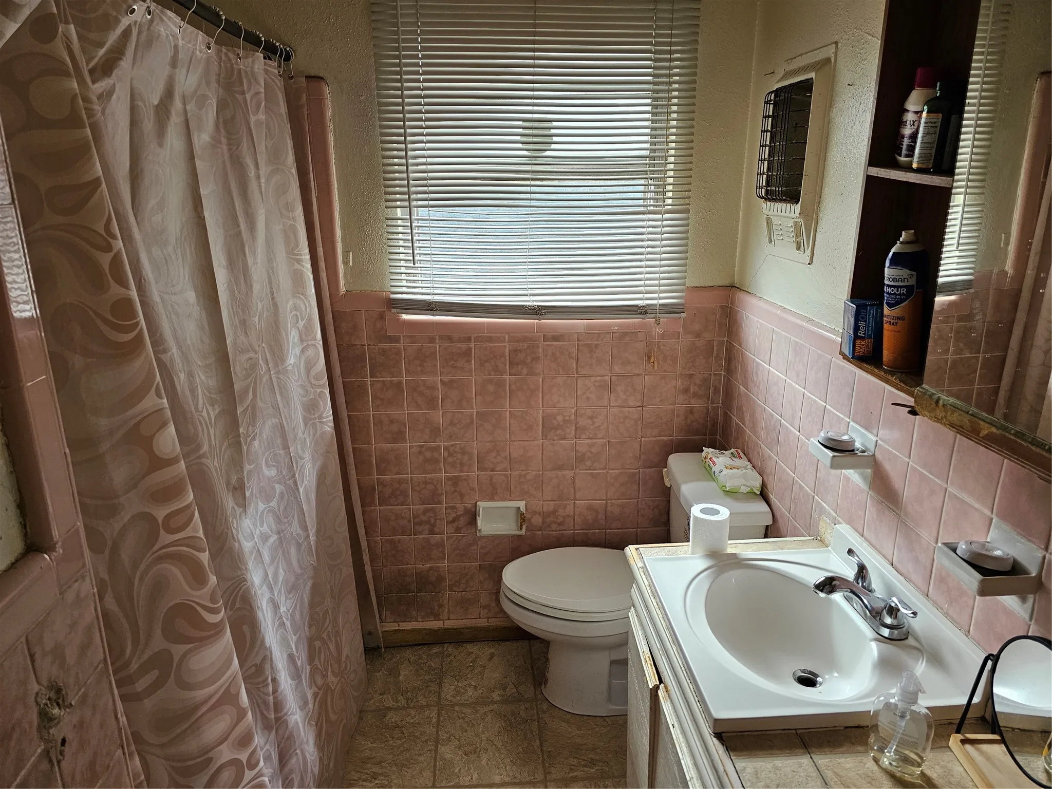 Bathroom featuring pink tiled walls, a white toilet, a single vanity with a white basin and chrome faucet, and a window with horizontal blinds