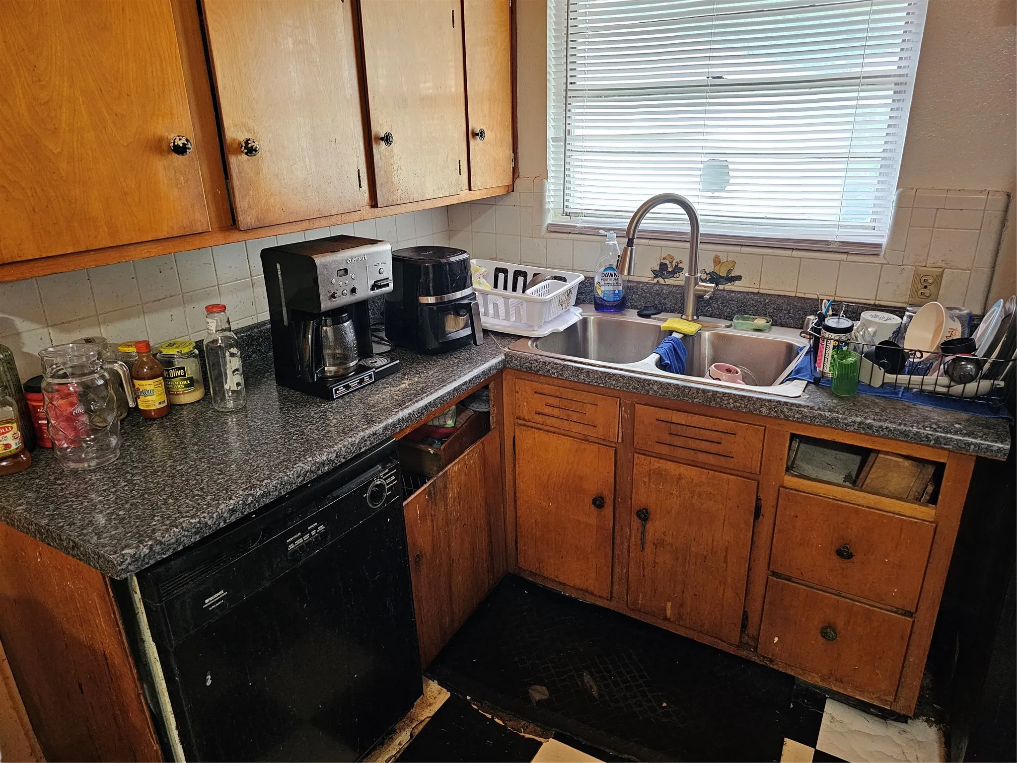 Kitchen featuring wood cabinetry, speckled countertops, a double basin stainless steel sink with a high-arc faucet, a window with blinds, and a built-in dishwasher