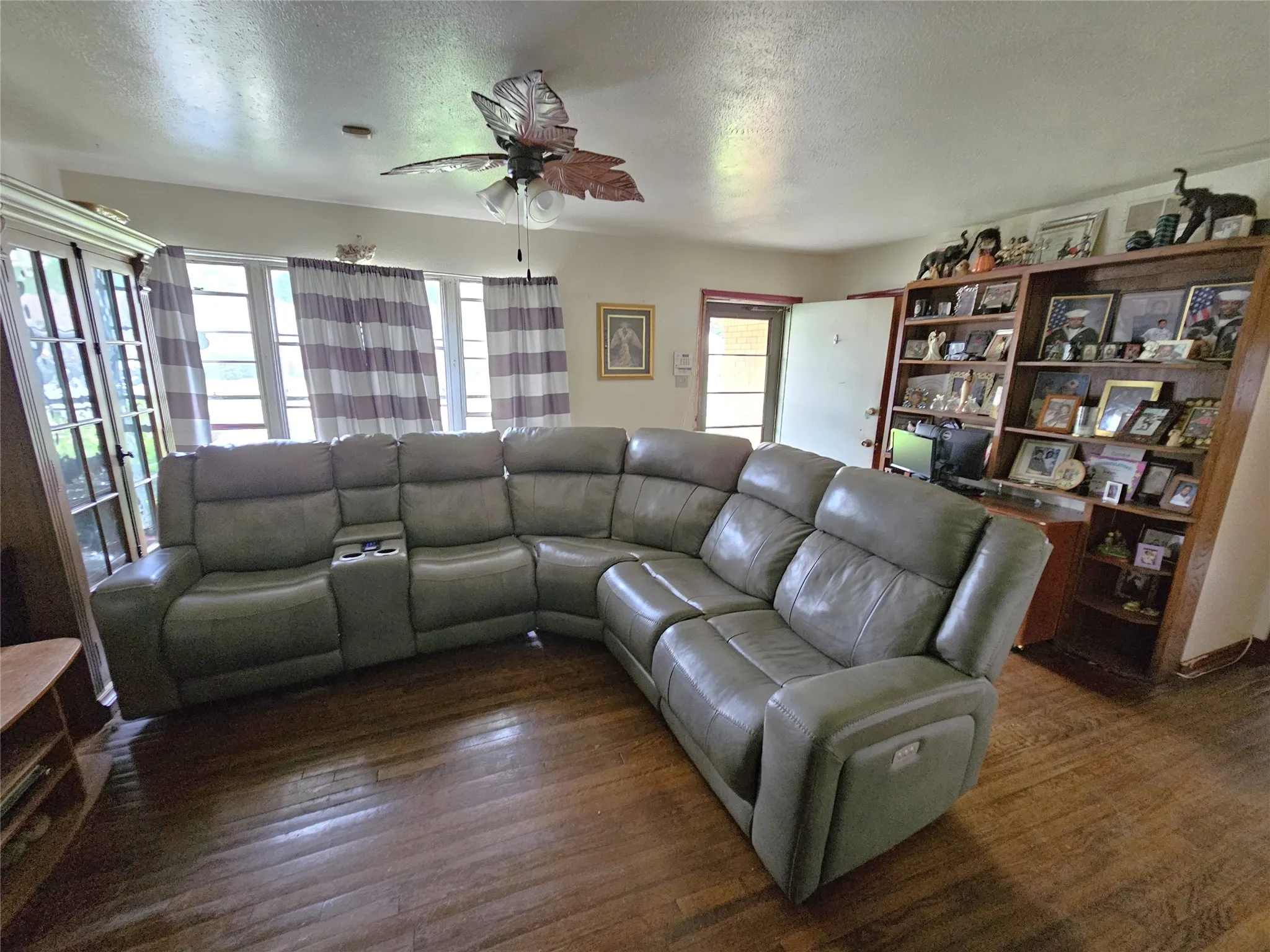 Spacious interior room featuring wood-finish flooring, a decorative ceiling fan, and multiple windows allowing natural light