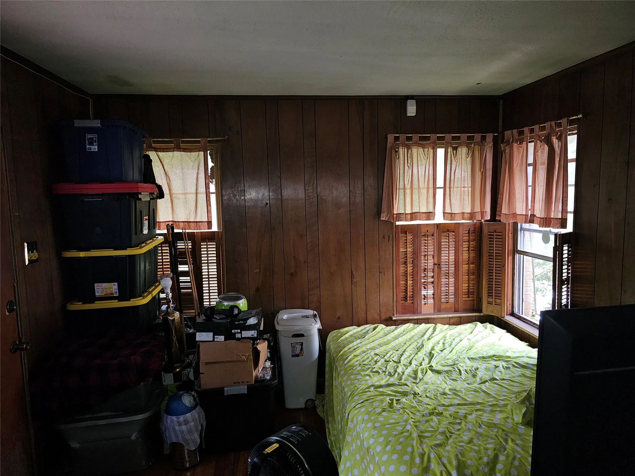 Room featuring wood-finish paneling, multiple windows with louvered shutters, and a white ceiling