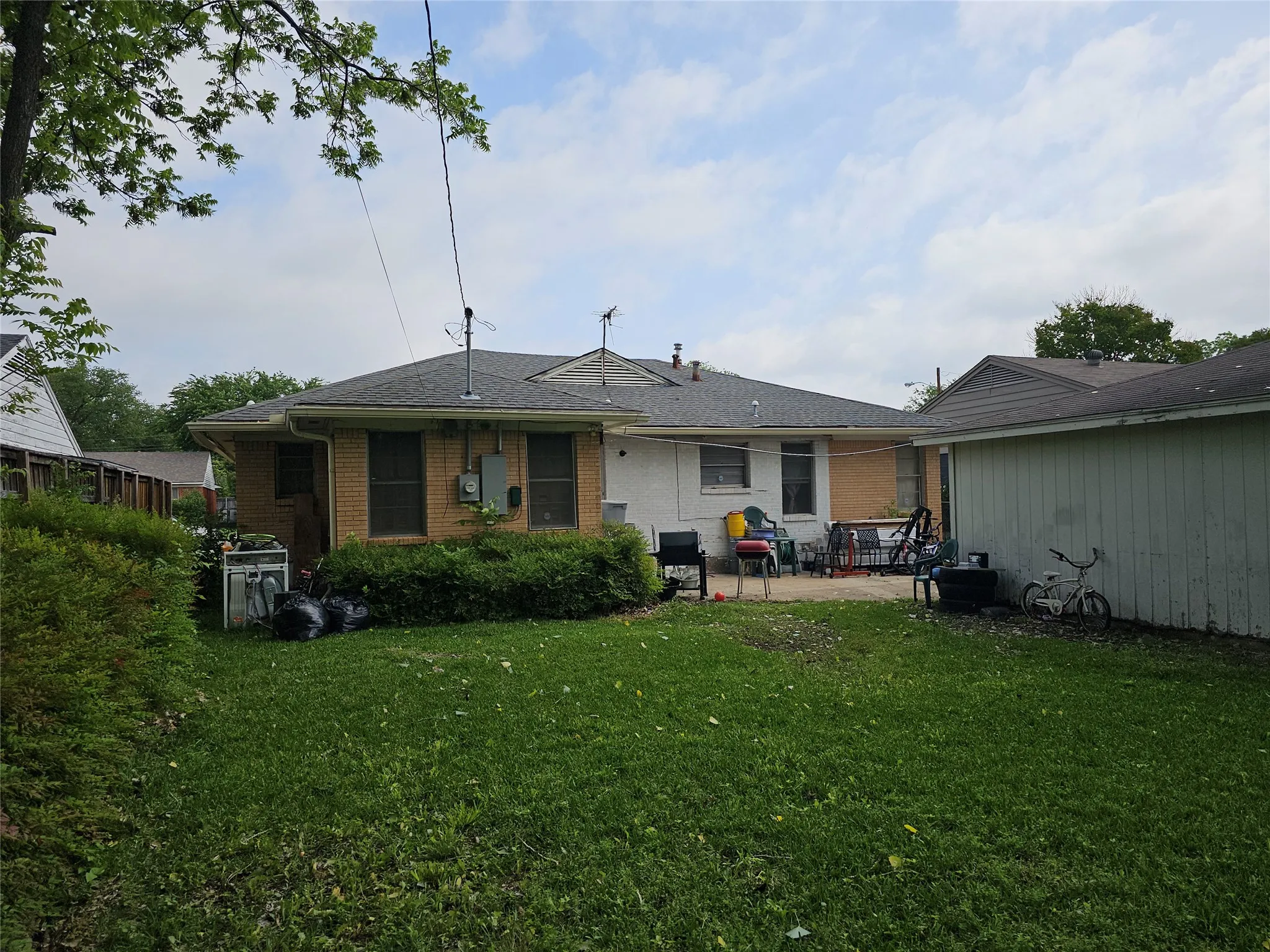 Rear exterior featuring a grass lawn, a paved patio area, and a detached building