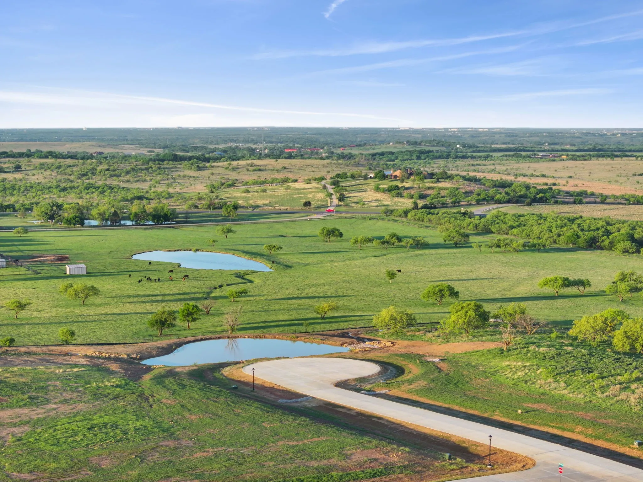 Expansive rural landscape featuring two ponds, verdant fields, scattered mature trees, and a paved roadway