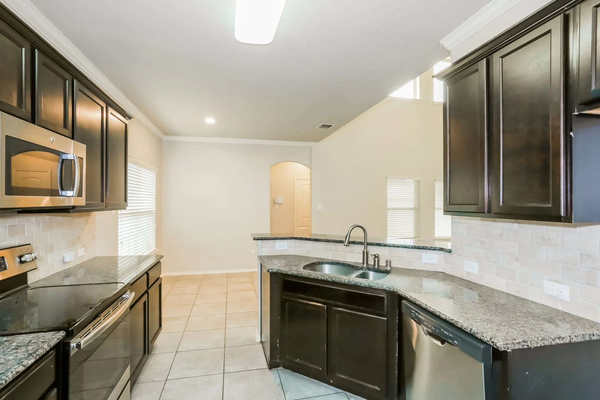 Kitchen featuring dark wood cabinetry, granite countertops, tile backsplash, stainless steel appliances, and tile flooring