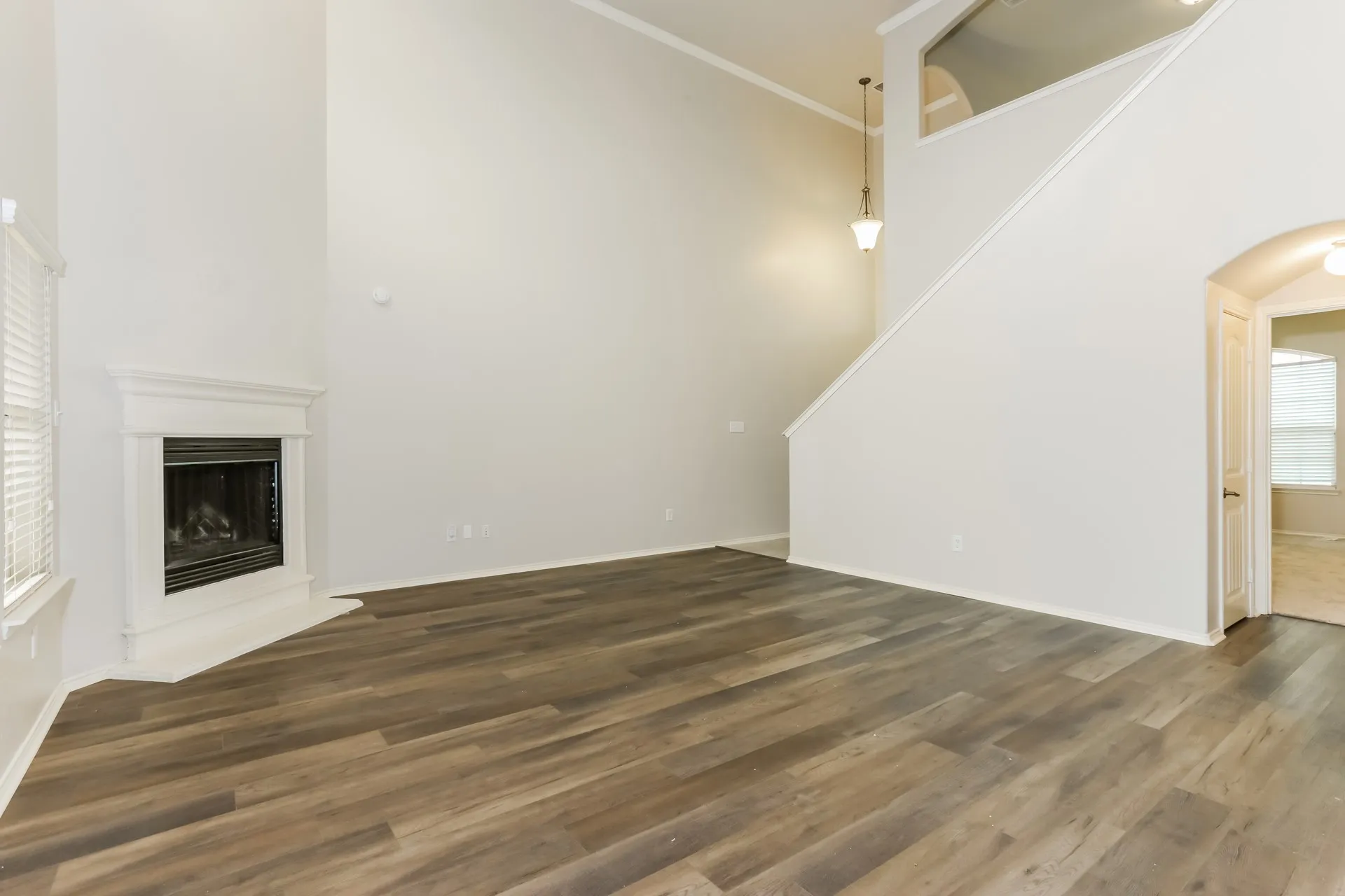 Spacious living area featuring wood-finish flooring, a corner fireplace with white mantel, vaulted ceilings, and an arched doorway