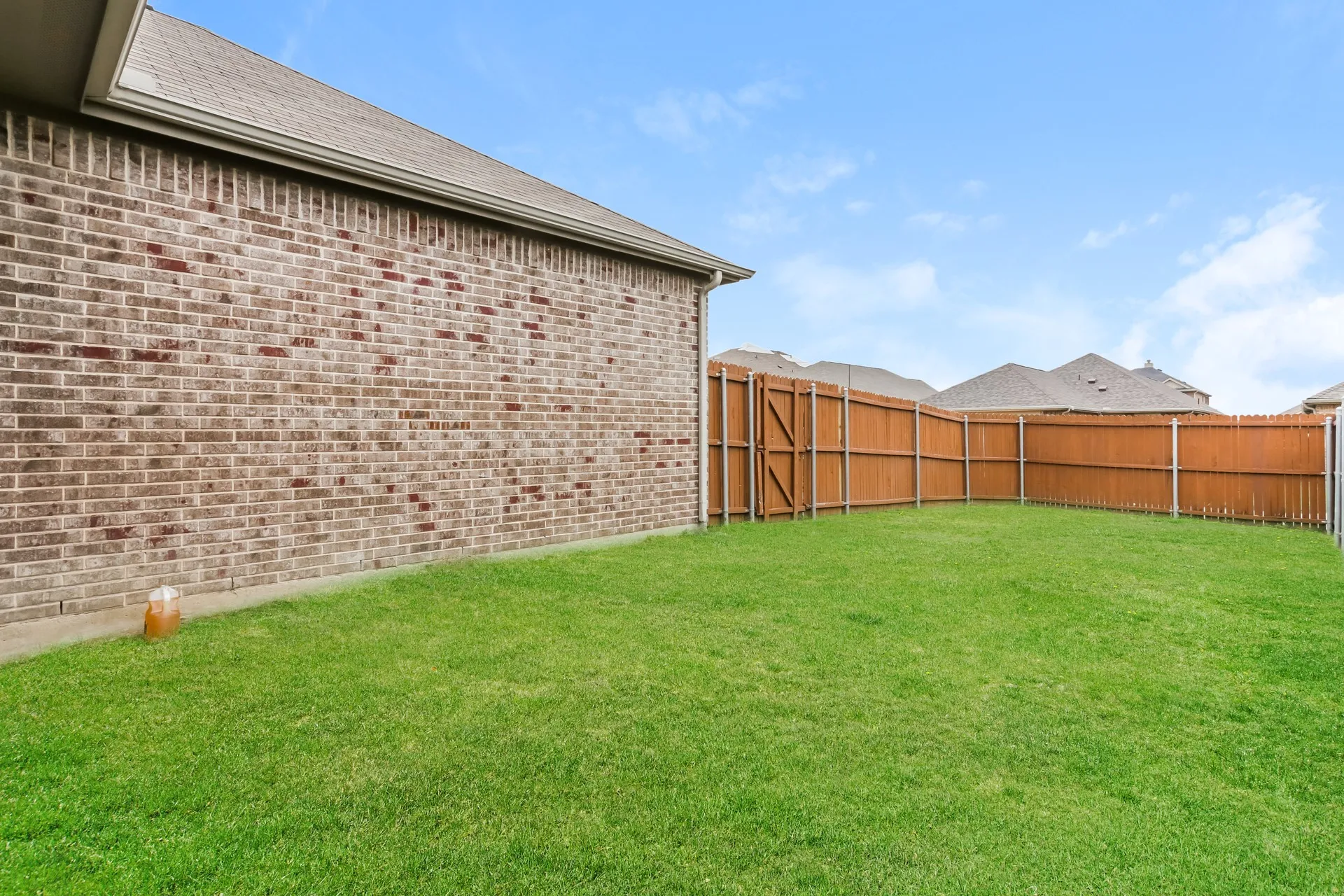 Expansive green lawn surrounded by a privacy fence, brick exterior, and a visible roofline
