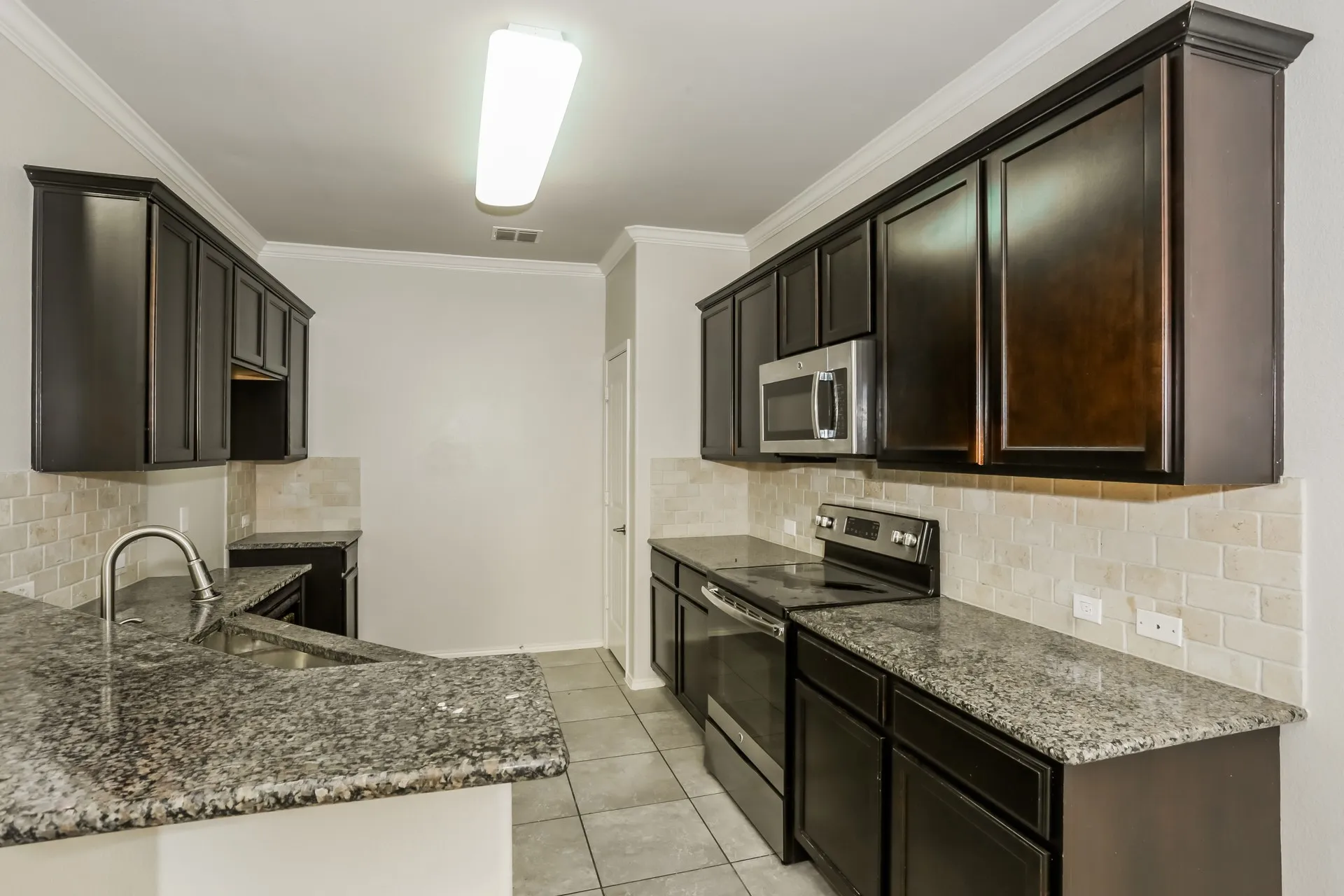 Kitchen featuring dark wood cabinetry, speckled countertops, stainless steel appliances, a tile backsplash, and tile flooring