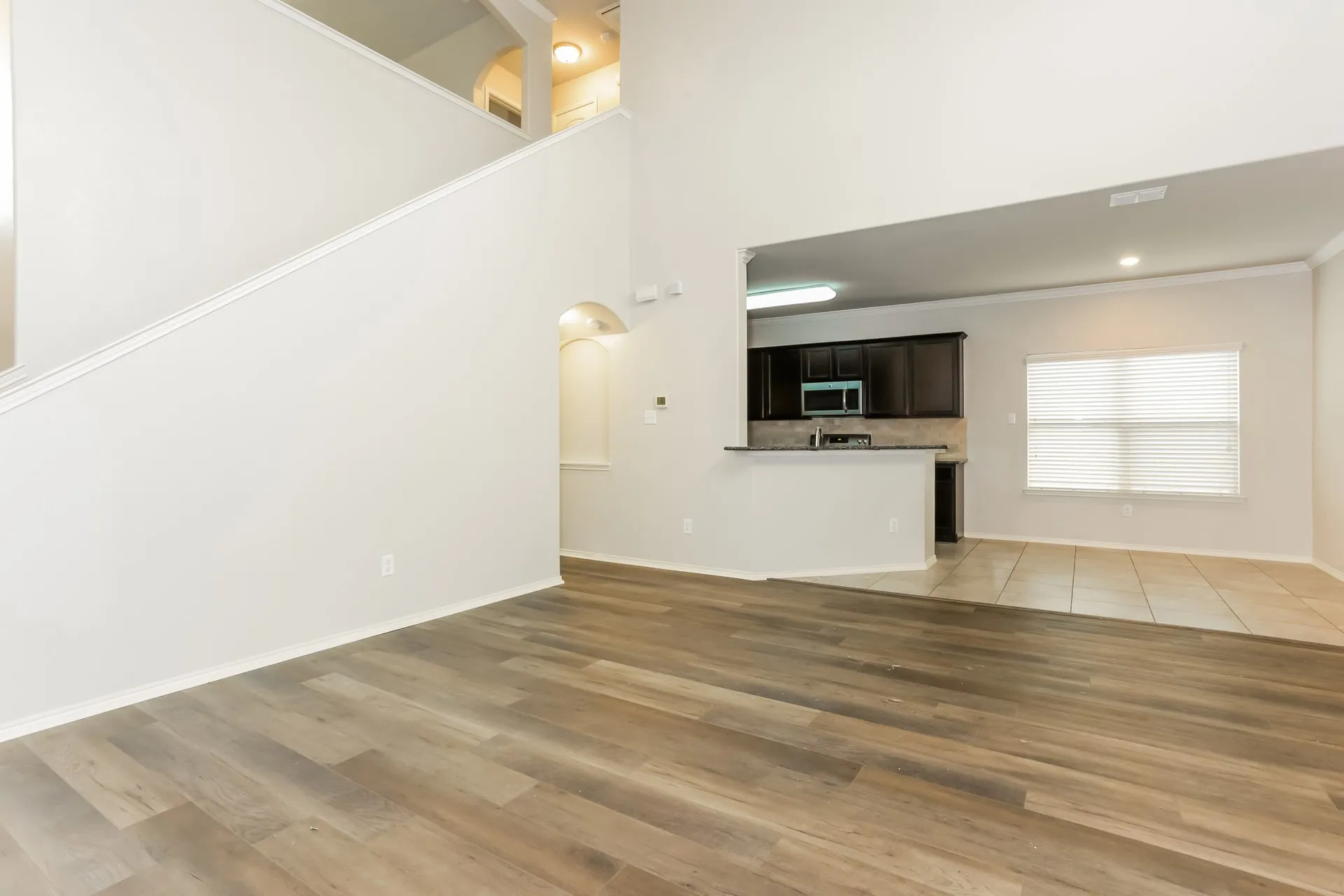 Spacious open-concept living area featuring wood-finish flooring, a neutral color palette, and high ceilings