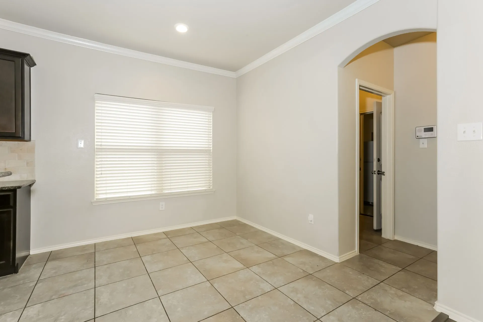 Spacious room featuring neutral wall paint, crown molding, a large window with blinds, and square tile flooring