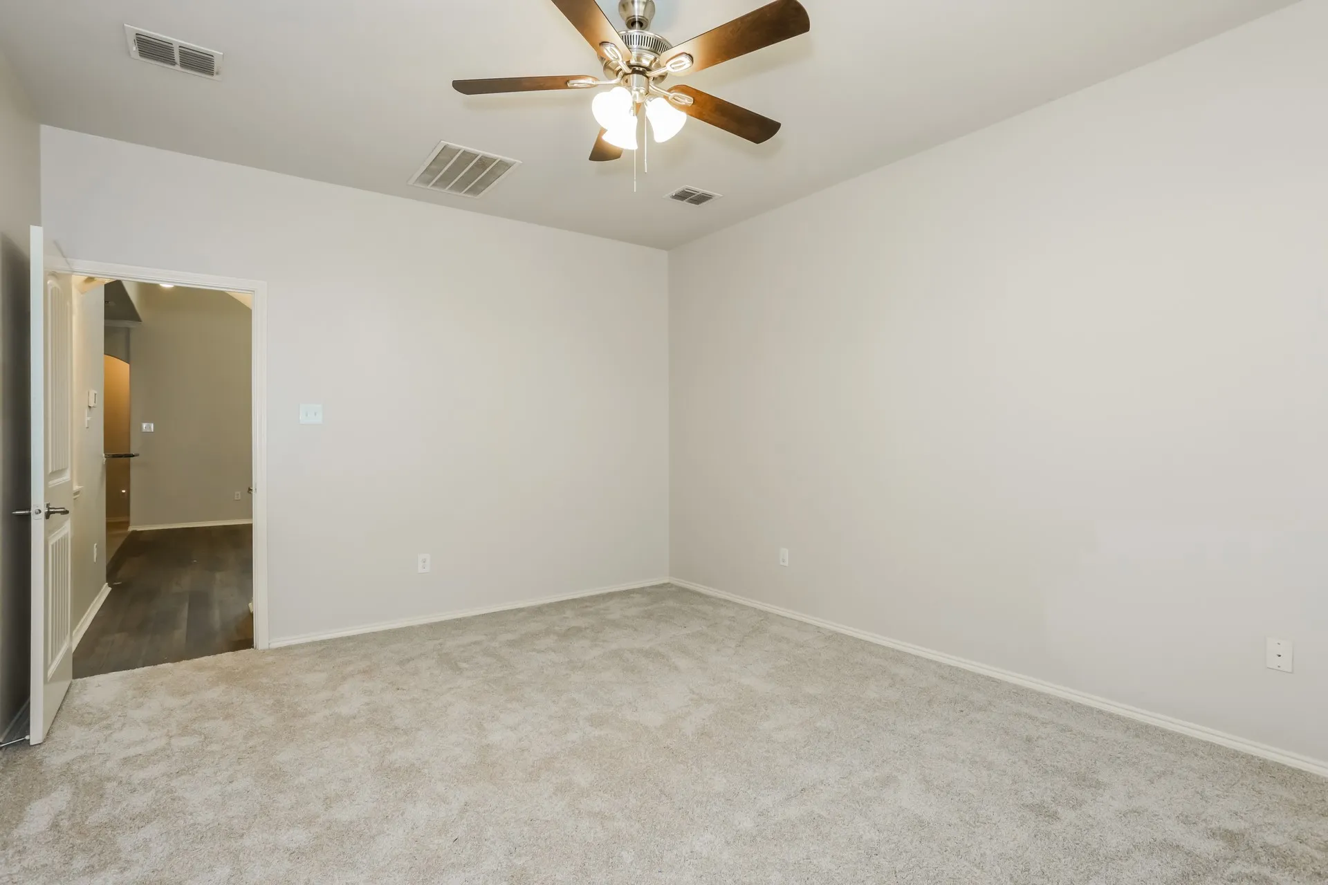 Spacious room featuring light-colored carpeting, neutral wall paint, and a ceiling fan with light fixture