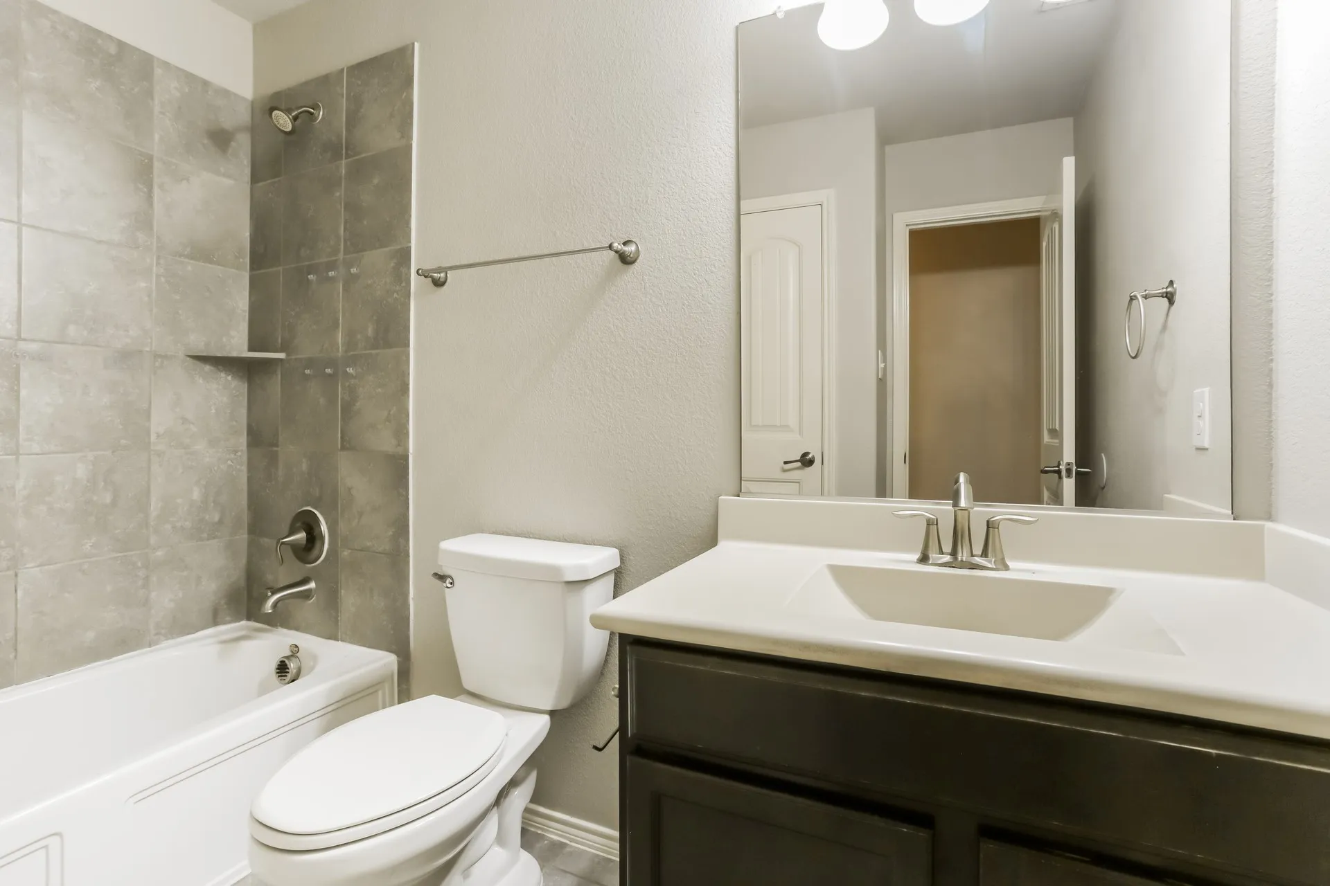 Full bathroom with a tub/shower combination, gray tile surround, and a built-in shower shelf