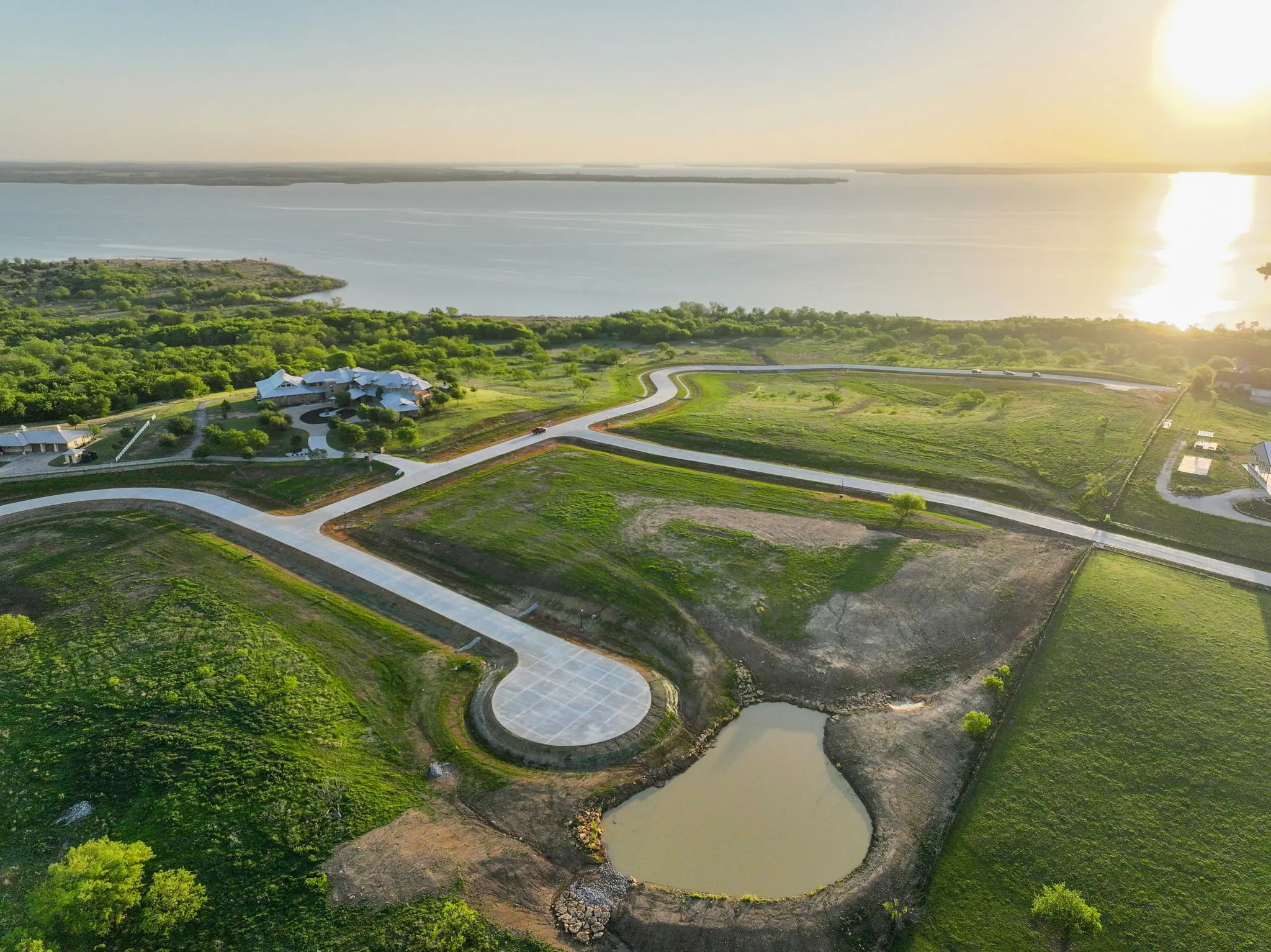 Expansive land parcel featuring paved roads, partially developed cul-de-sac, and a small pond