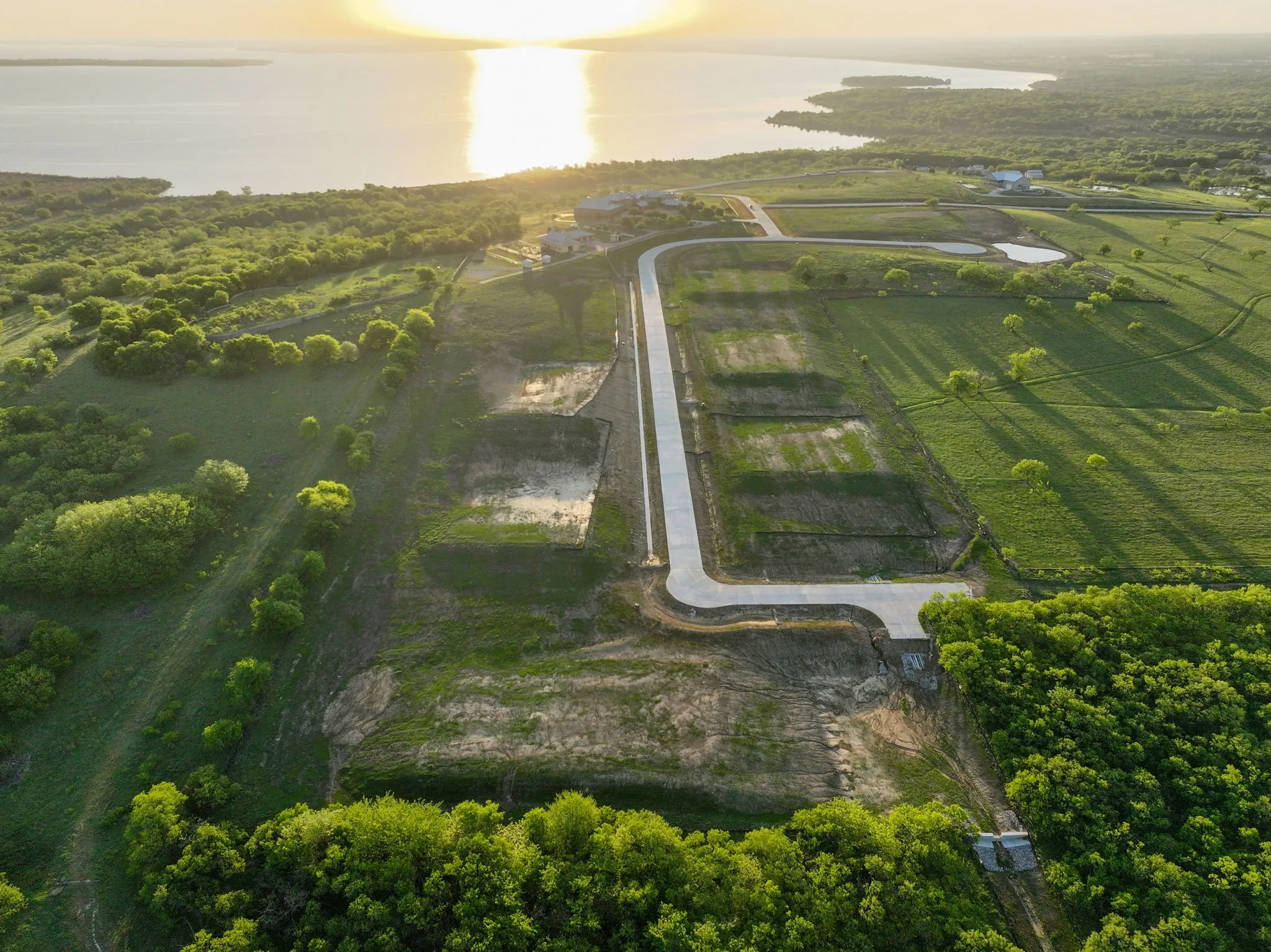Expansive land parcels featuring cleared building sites, new road infrastructure, and a substantial body of water in the background